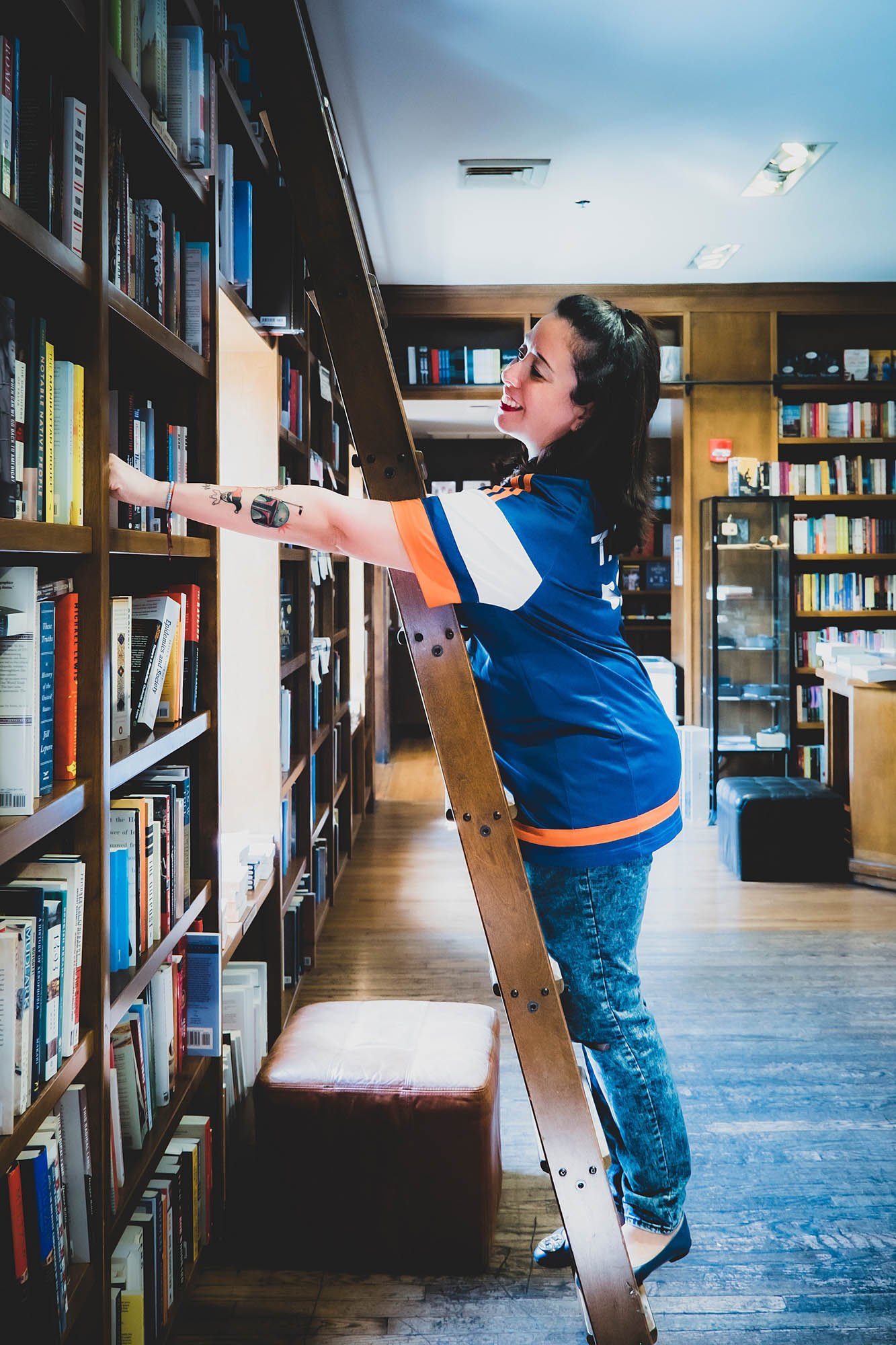 small business owner grabbing book off of shelf in bookstore taken by Sharma Shari Photography