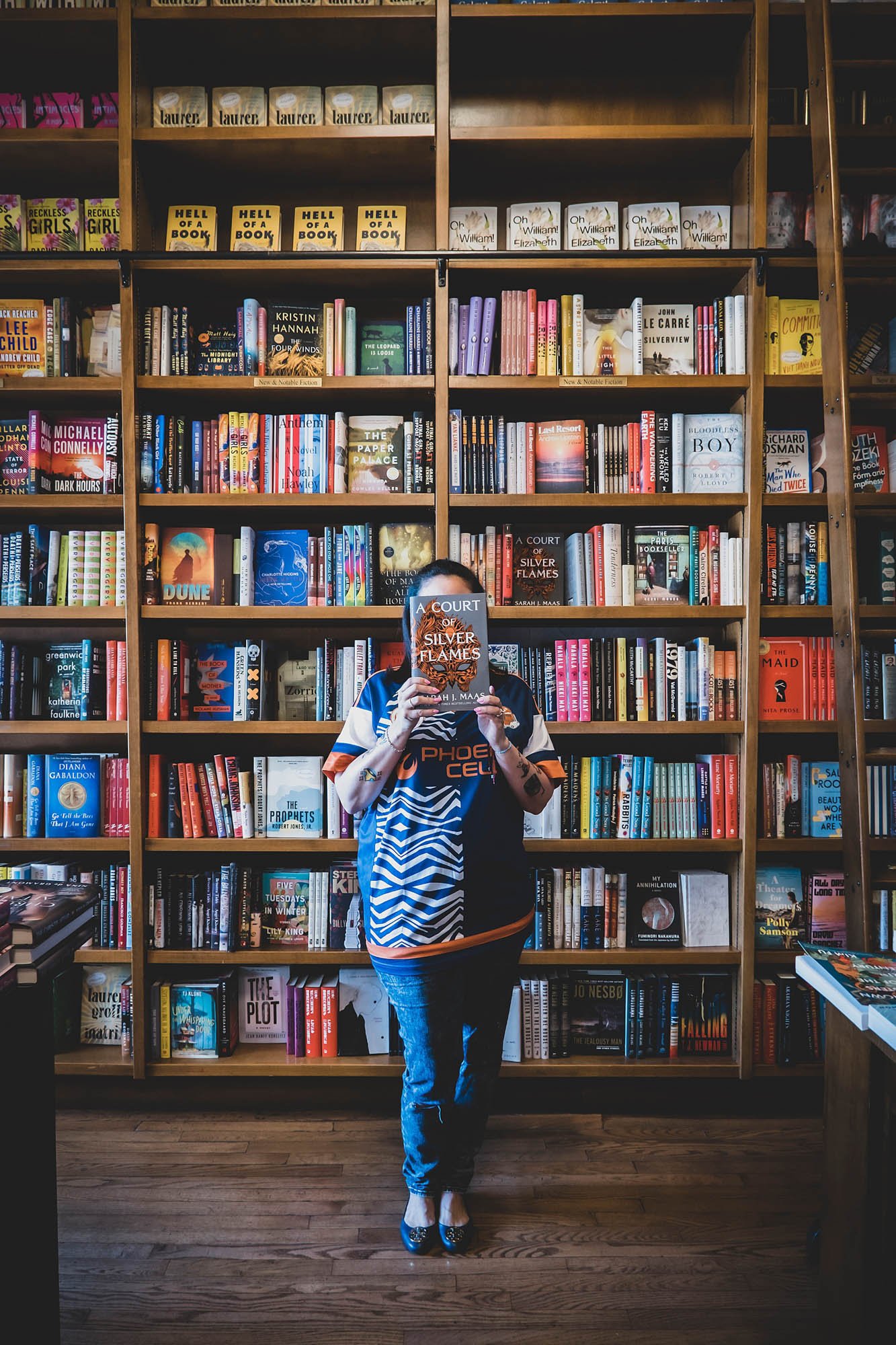 small business portrait of owner holding up a book in front of her face at book shop taken by Sharma Shari Photography