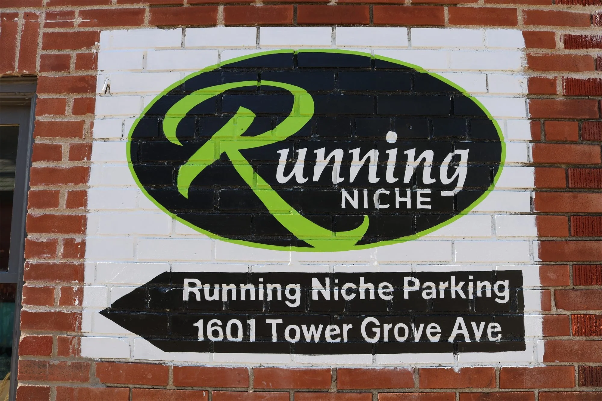 Painted brick Running Niche parking sign pointing to the lot at 1601 Tower Grove Ave, St. Louis