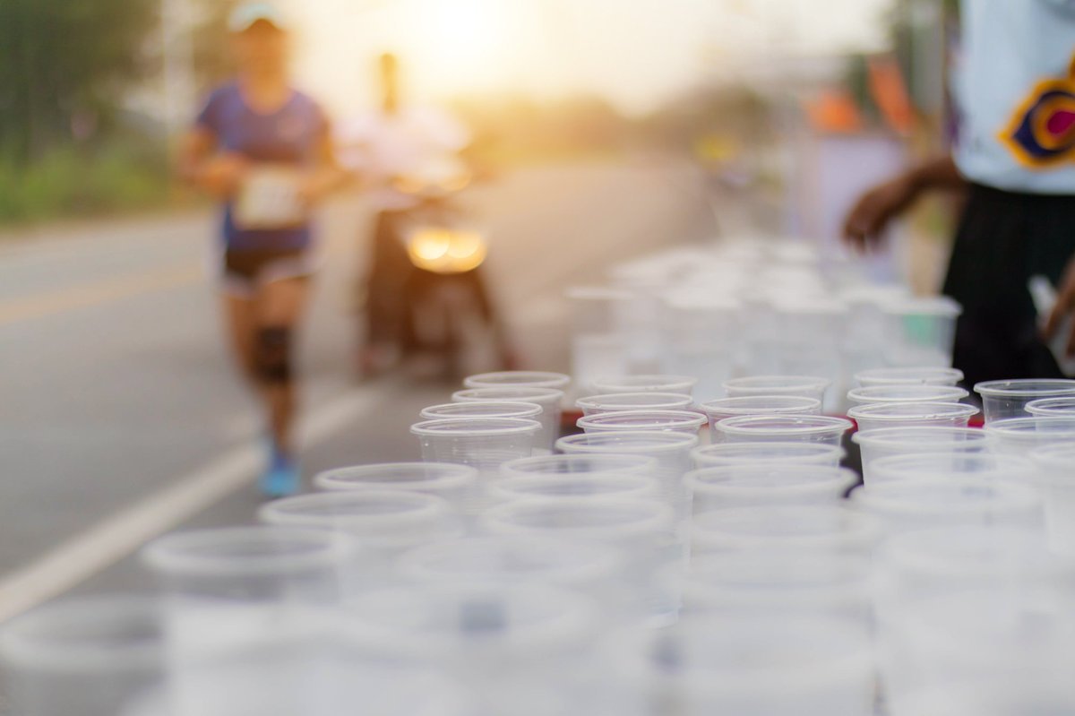 Marathon aid station cups lined up with runners approaching in golden hour light during race