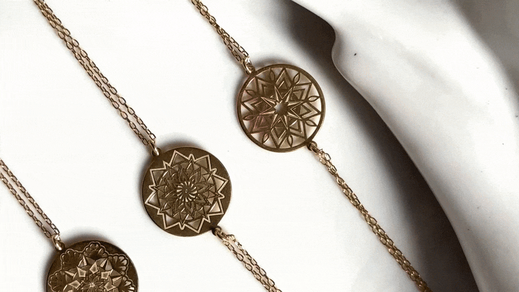 Three gold necklaces with circular pendants featuring intricate geometric designs, laid out on a white surface.