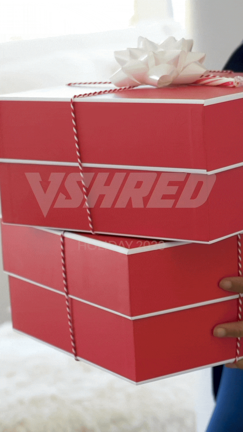 A person holding three stacked red gift boxes with white trim, tied with white and red twine, topped with a white ribbon bow.