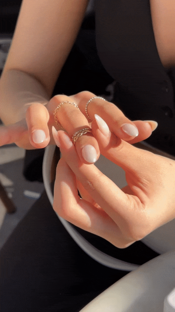 Close-up of a woman’s hands displaying multiple rings, with light-colored nail polish, resting on her lap.