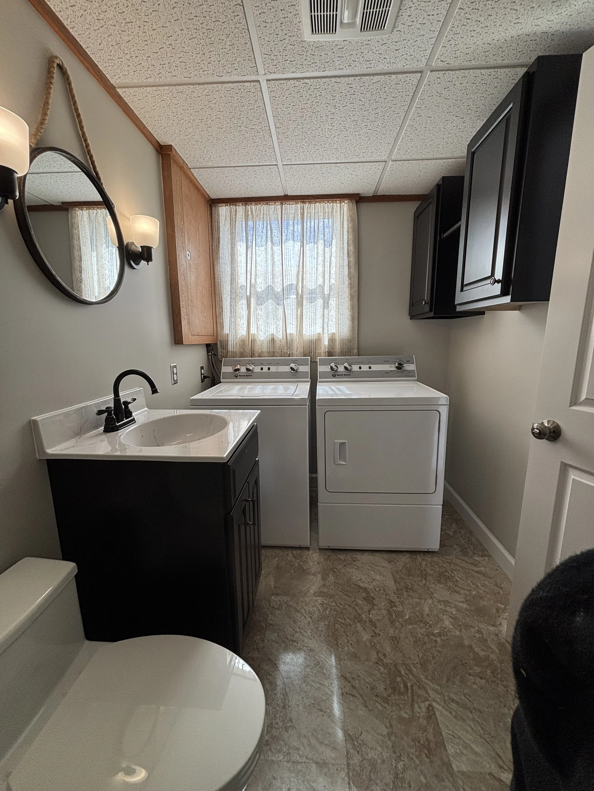Laundry and utility room renovation in Lancaster County featuring a new utility sink, vanity, toilet, sconce lighting, cabinets, LVP flooring, drop ceiling, trim, and paint.