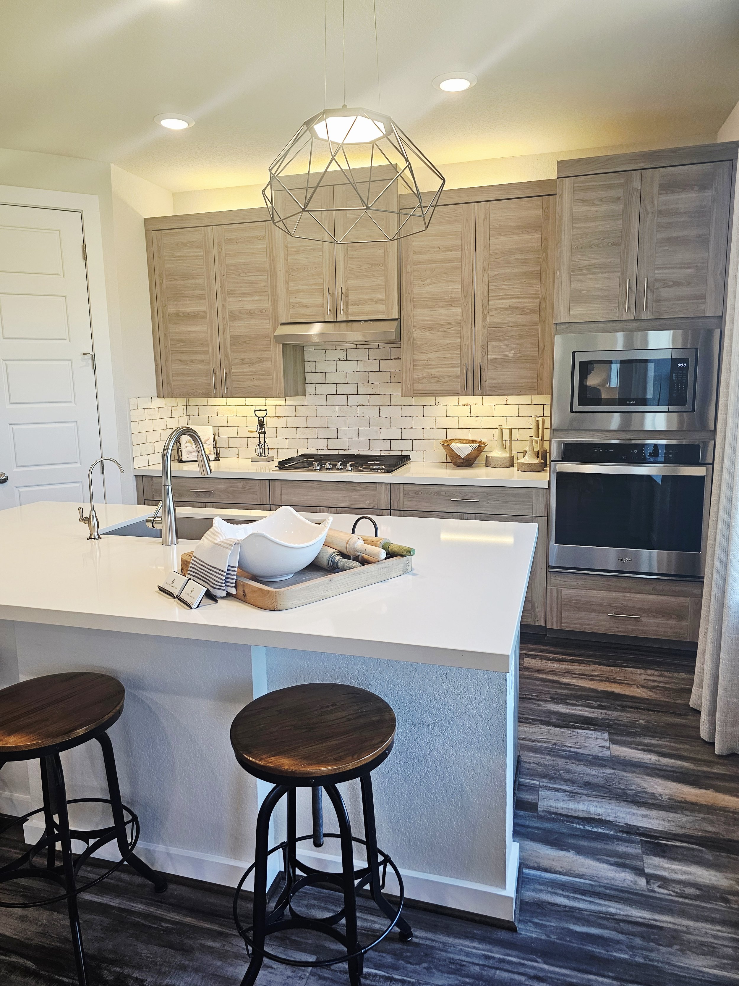 Modern kitchen with light wooden cabinets, white subway tile backsplash, stainless steel appliances, and a white kitchen island with dark wooden stools.