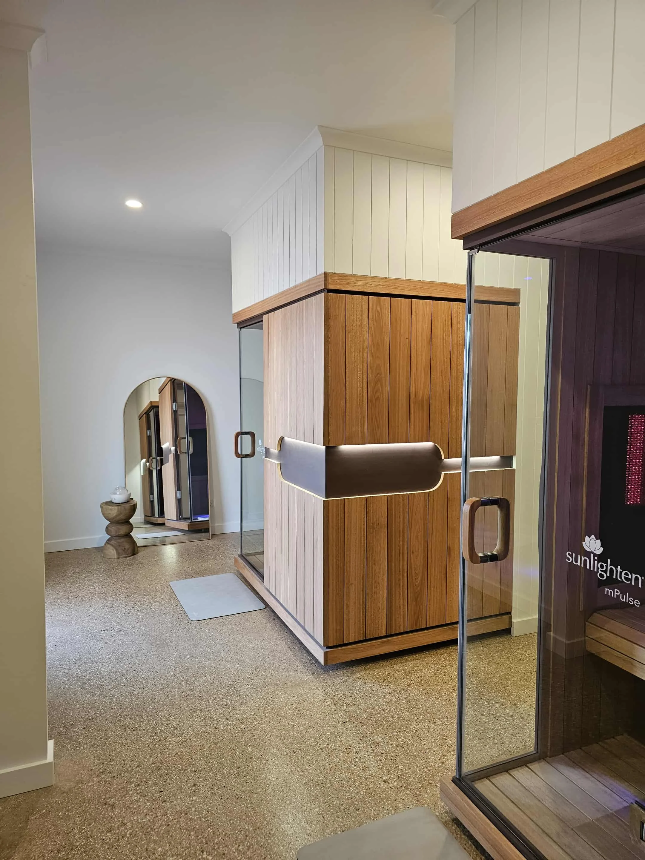 Interior of a wellness or spa room featuring a wooden sauna with glass door, a small mirror on the wall, and a textured carpeted floor.