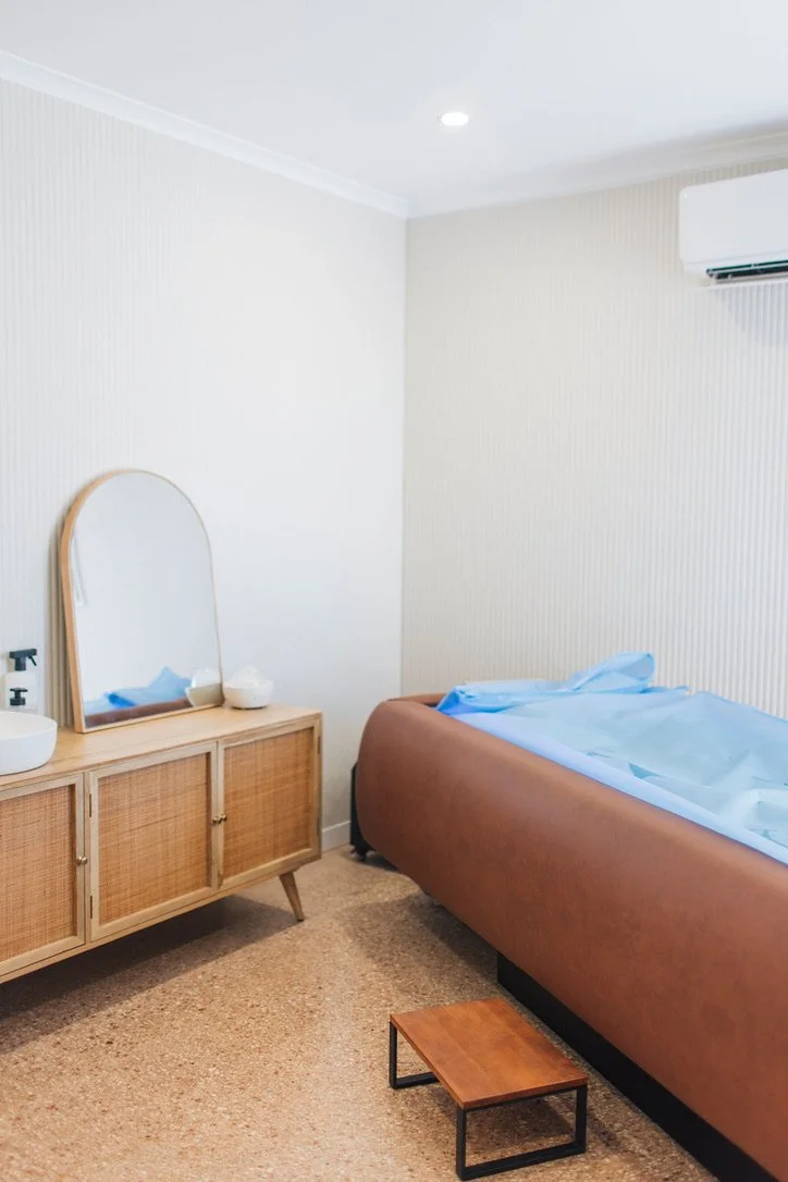 ice bed, a wooden dresser with a mirror, a small wooden stool, and minimal decor.
