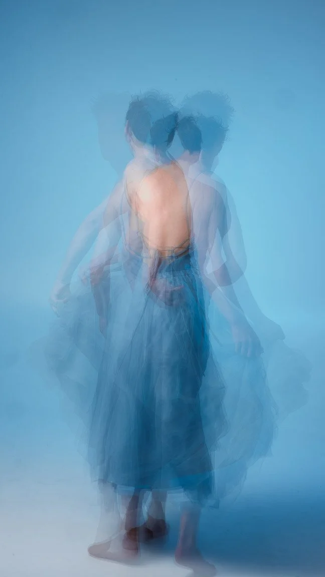 A man is captured twirling in a blue dress, creating a beautiful effect with motion blur from the long exposure. The image highlights the elegance of the costume design and portrays a sense of dynamic movement associated with dance.