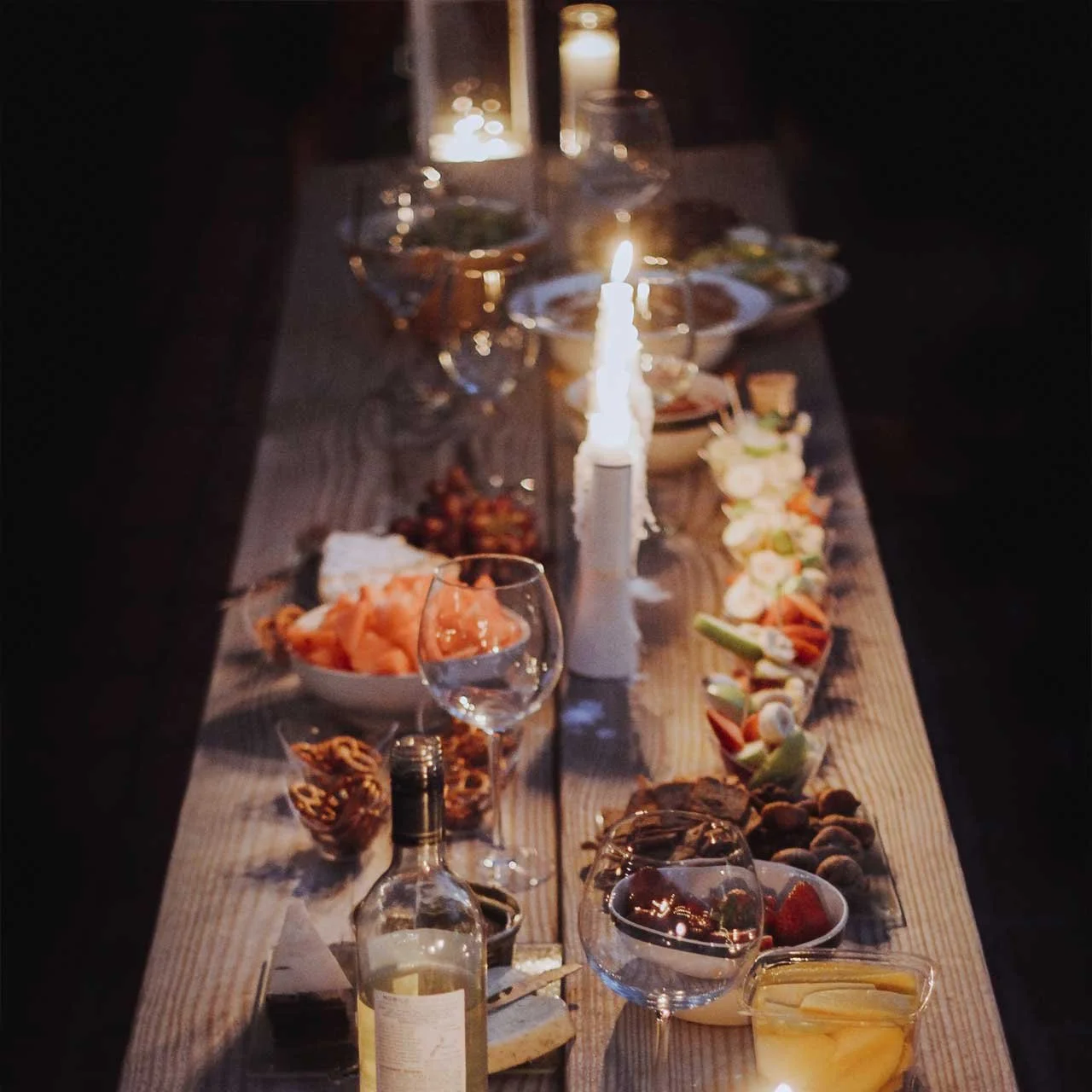 Candlelit table with wine, cheese, fruits, and snacks.