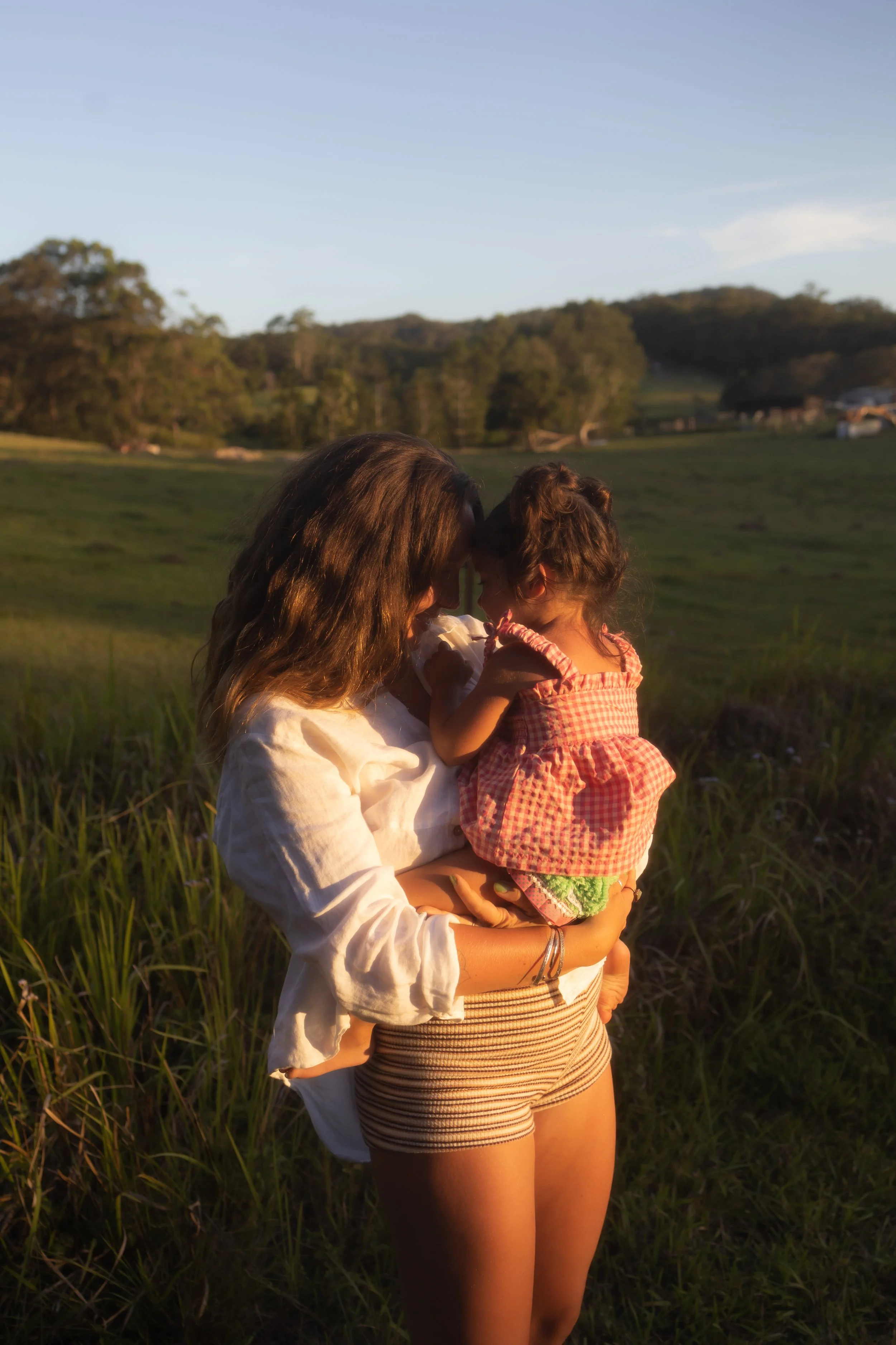 A newborn baby wearing a striped hat is sleeping on a person's arm, with the person’s hand gently holding the baby's arm.