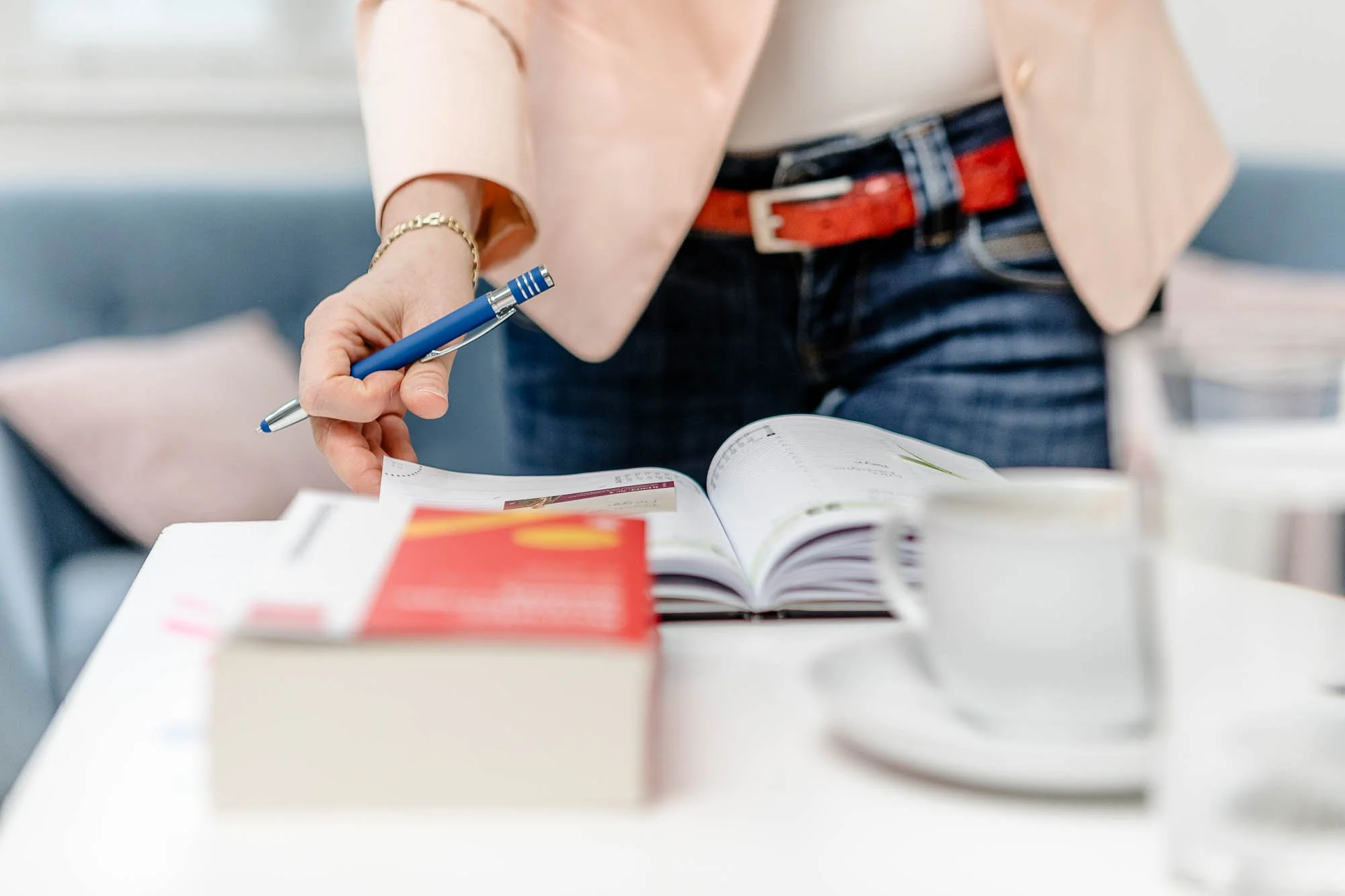 Eine Frau liest in einem offenen Buch auf einem Tisch, während sie einen Kugelschreiber in der Hand hält.