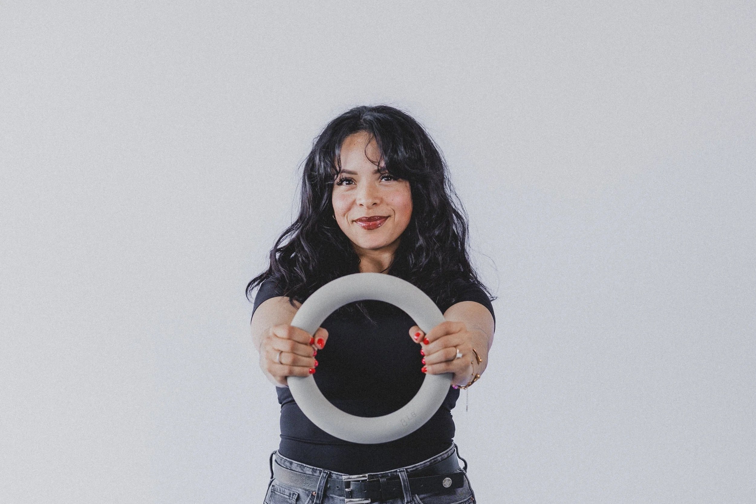 Fitness instructor holding a weighted pilates ring in front of a plain light gray background.