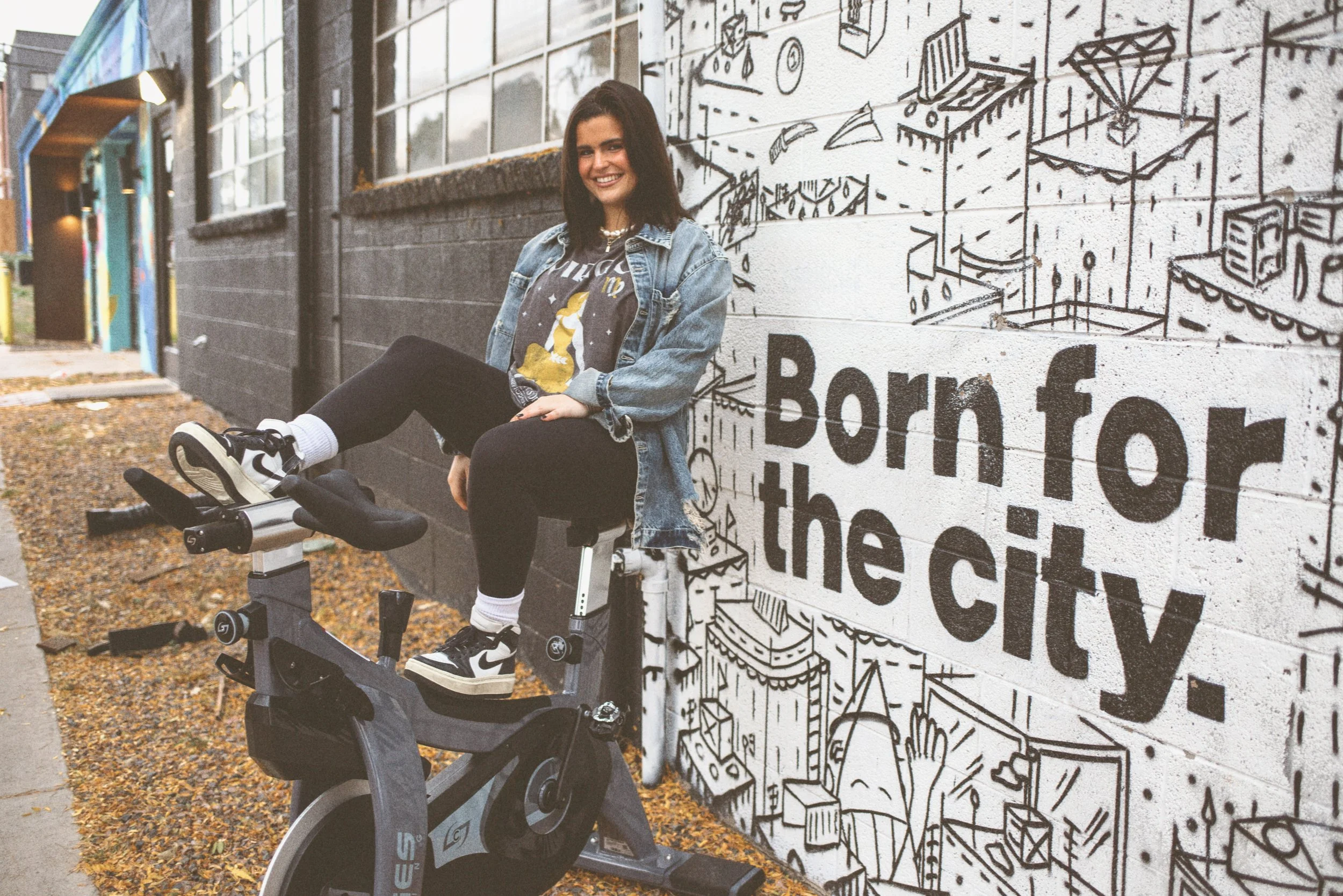 Person smiling on stationary bike next to a mural with the text 'Born for the city.'