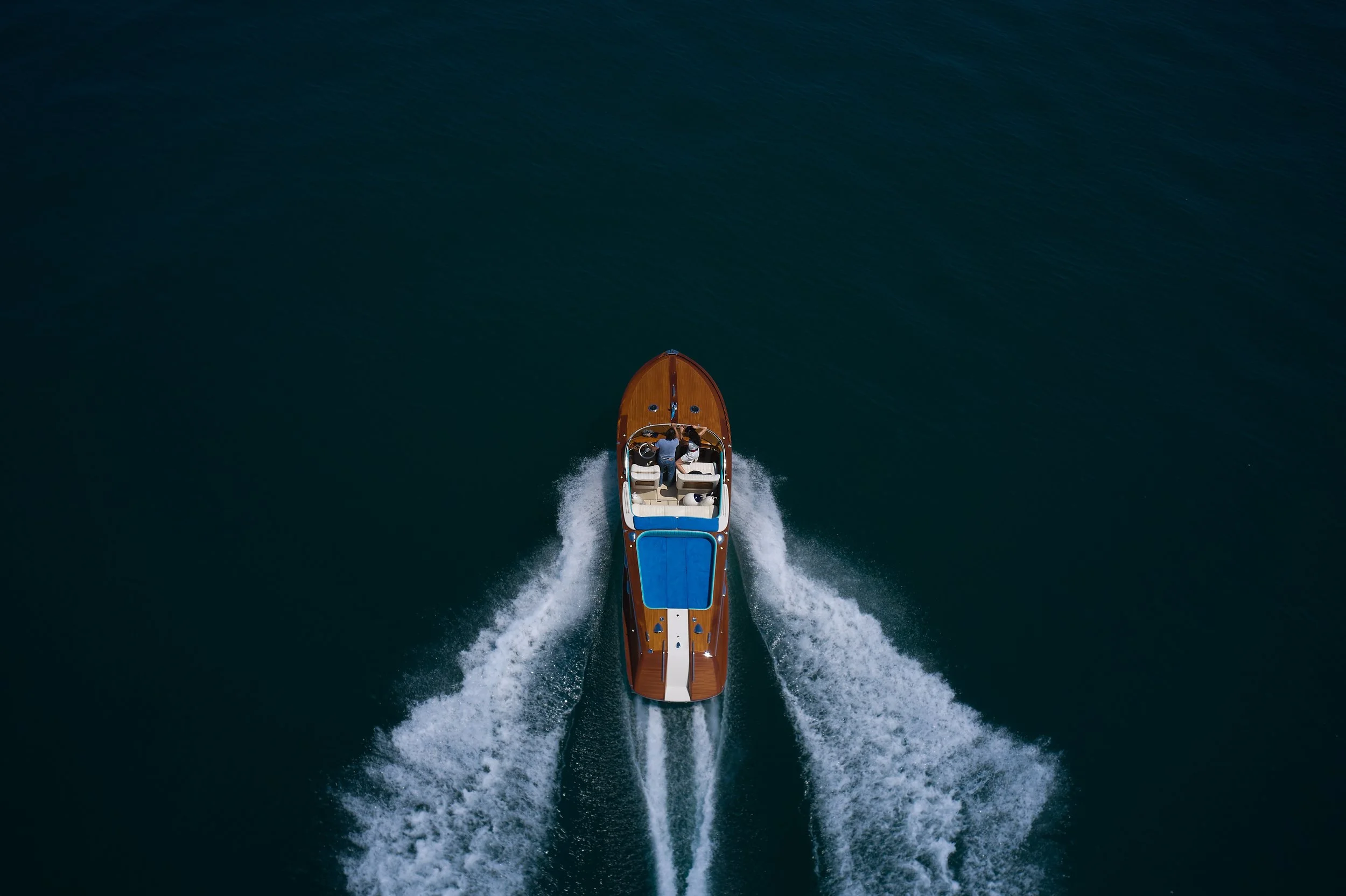 Aerial view of a yacht speeding through dark blue water, creating a wake behind it.