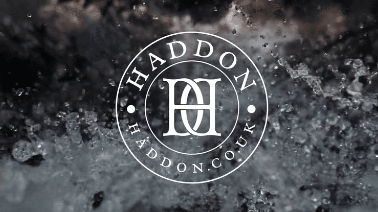 Haddon brand monogram in a circular lockup format, featuring a refined serif logo and domain text over a running water background – evoking English heritage and timeless luxury.