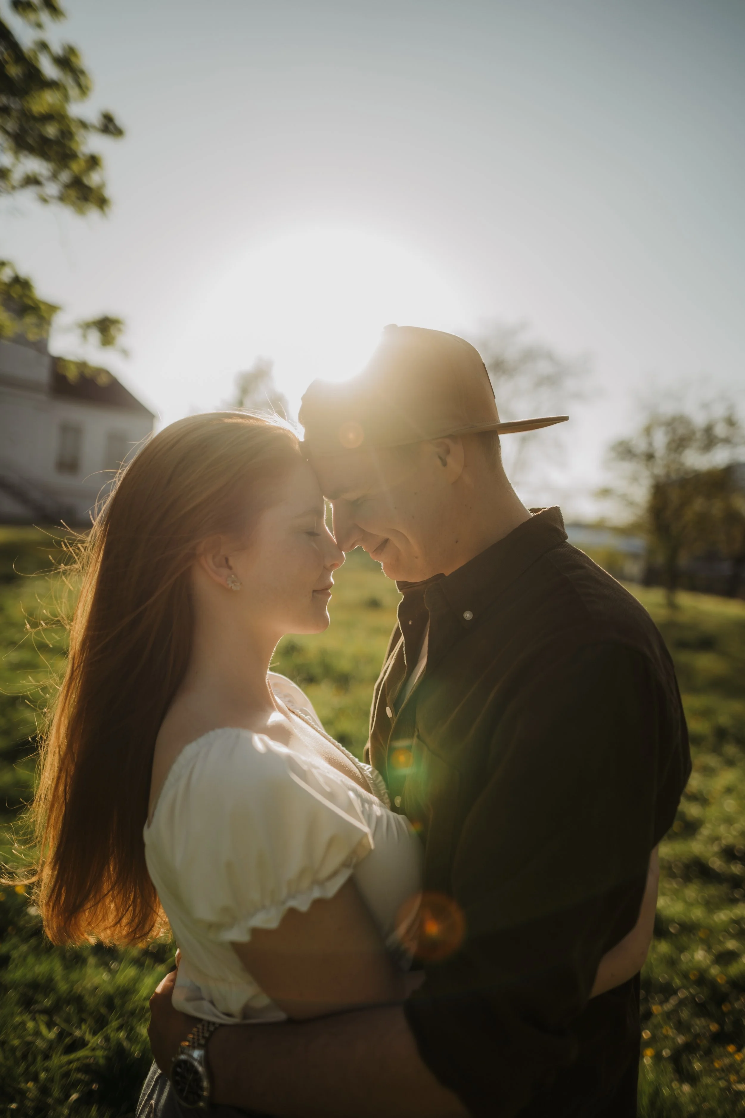 Ein junges Paar steht im Sonnenlicht, erkennt sich liebevoll, mit geschlossenen Augen, im Freien auf einem grünen Feld, der Sonnenuntergang im Hintergrund.