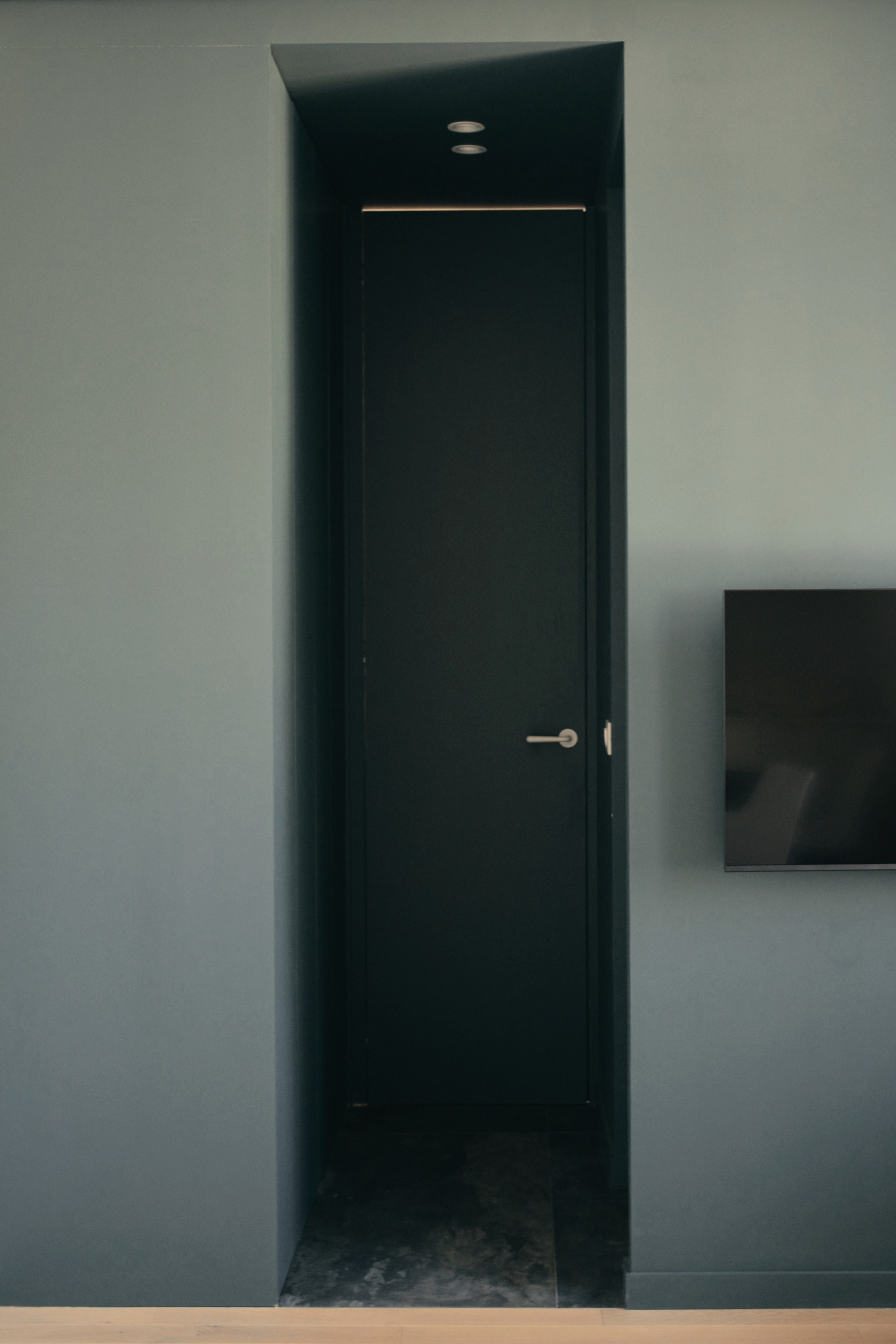 Une porte noire encastrée dans un mur gris, située à côté d'un téléviseur