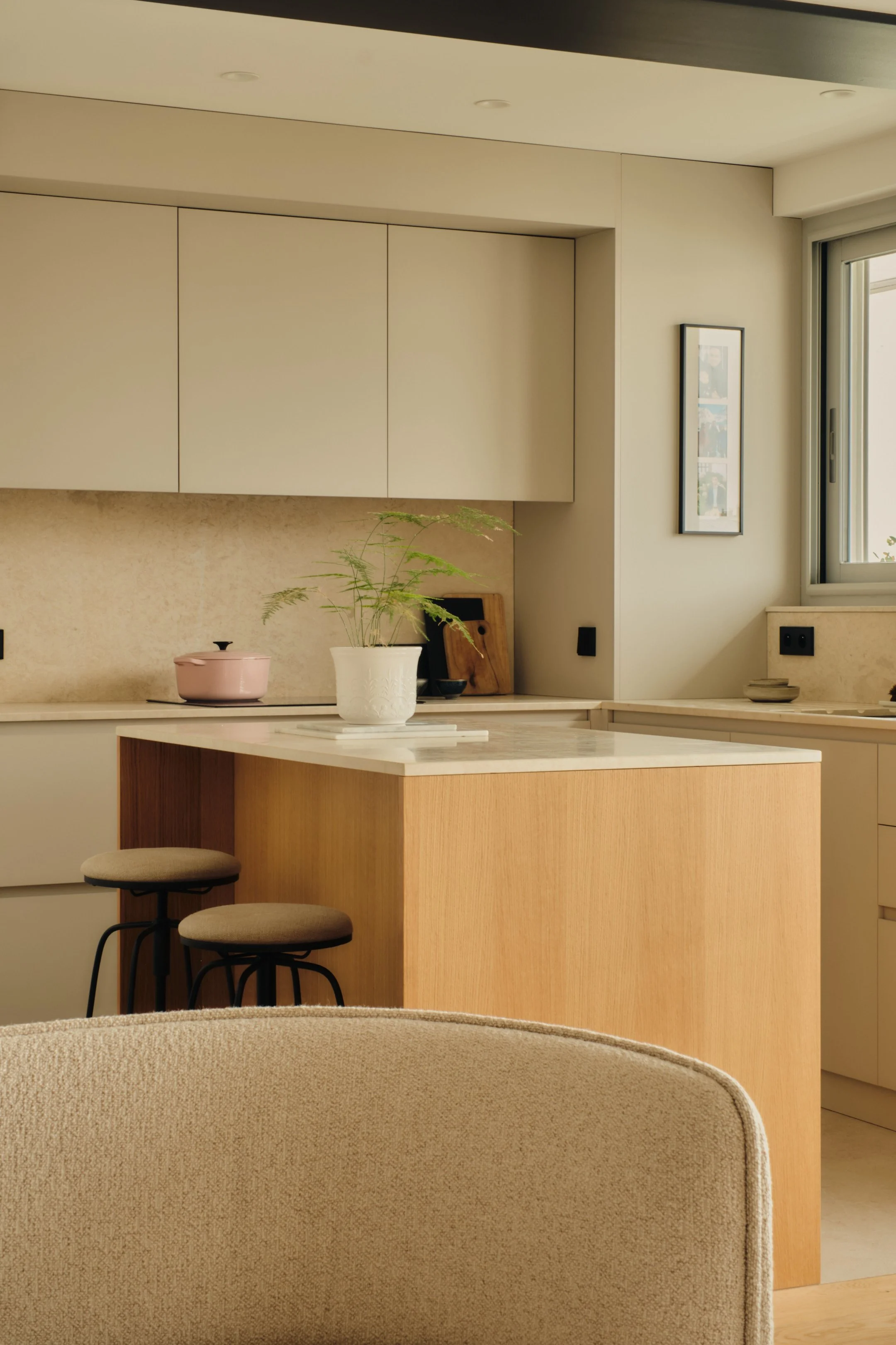 Cuisine moderne avec îlot en bois et plantes vertes, lumière naturelle, et décoration minimaliste.
