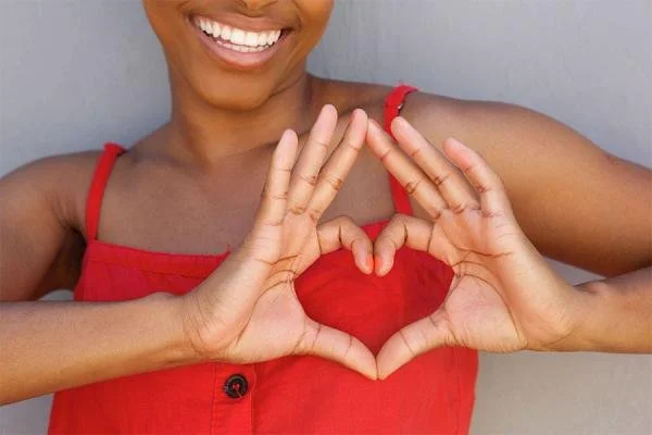 Person in a red top forming a heart shape with their hands in front of their chest.
