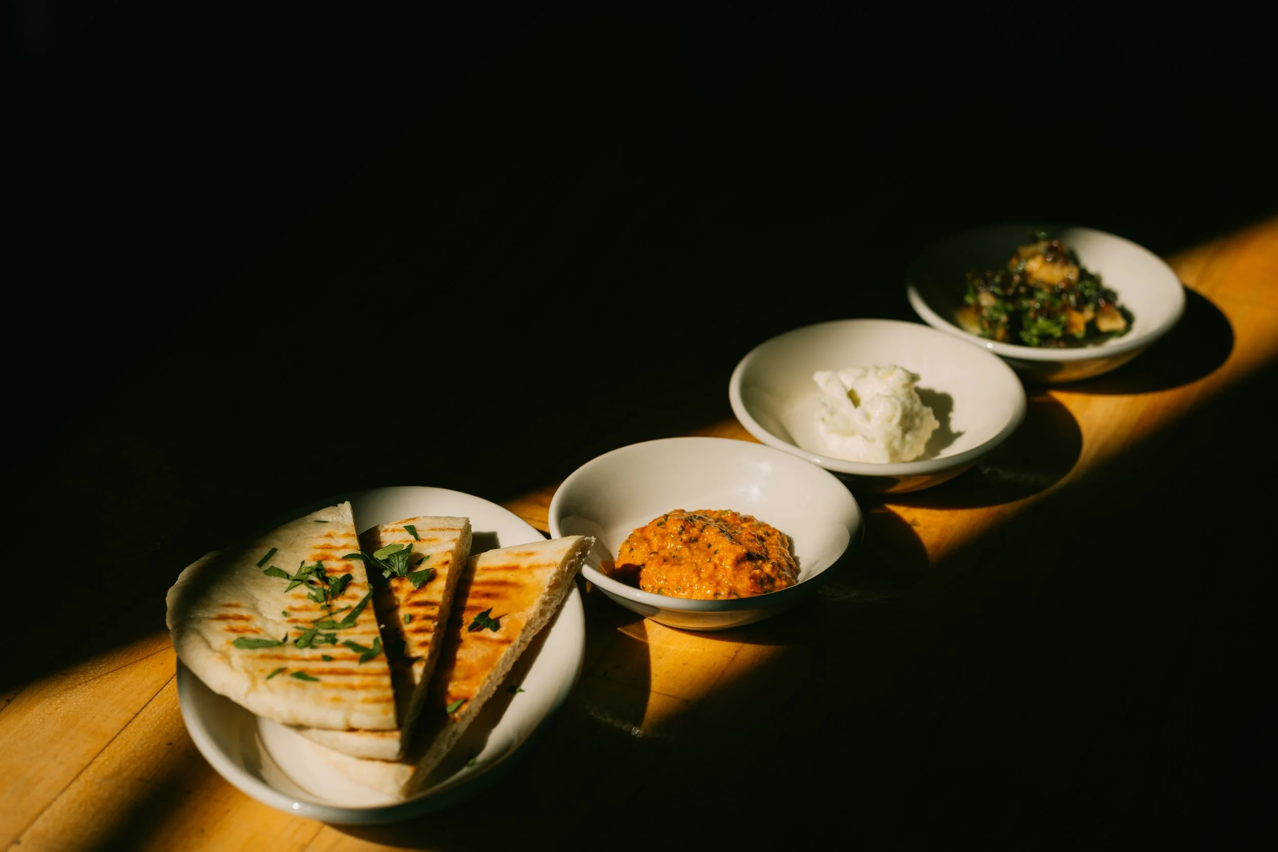 Assorted Indian dishes served in small white bowls on a wooden surface with dark background.