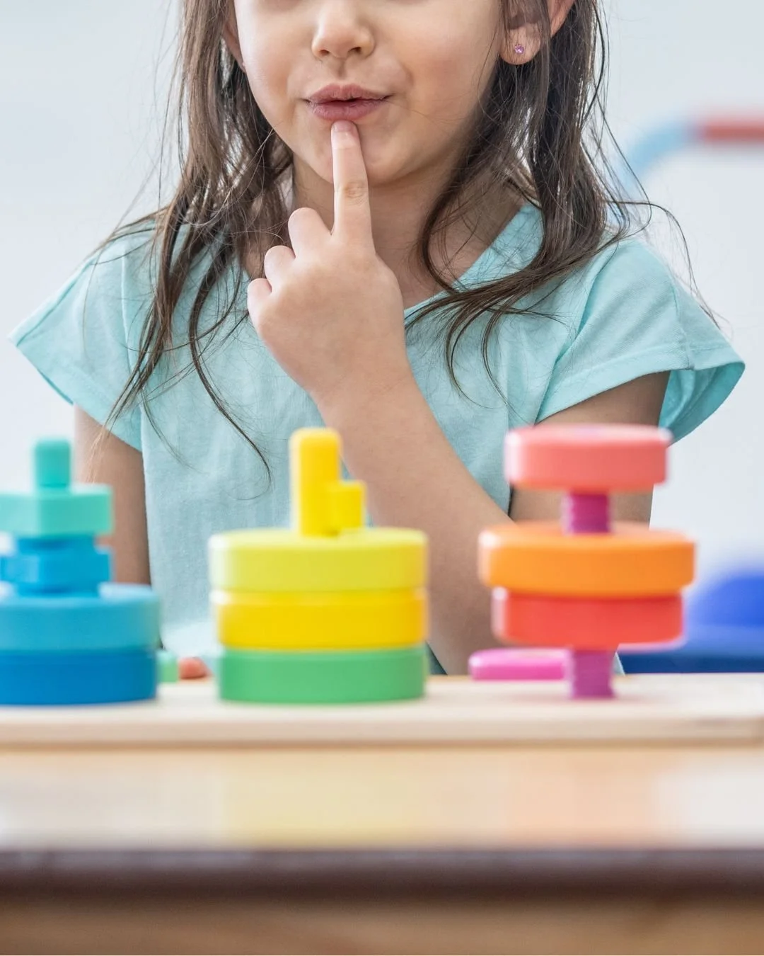 A young girl in speech therapy with stacking rings in front of her and her finger to her rounded lips, as though practicing the "oooo" sound