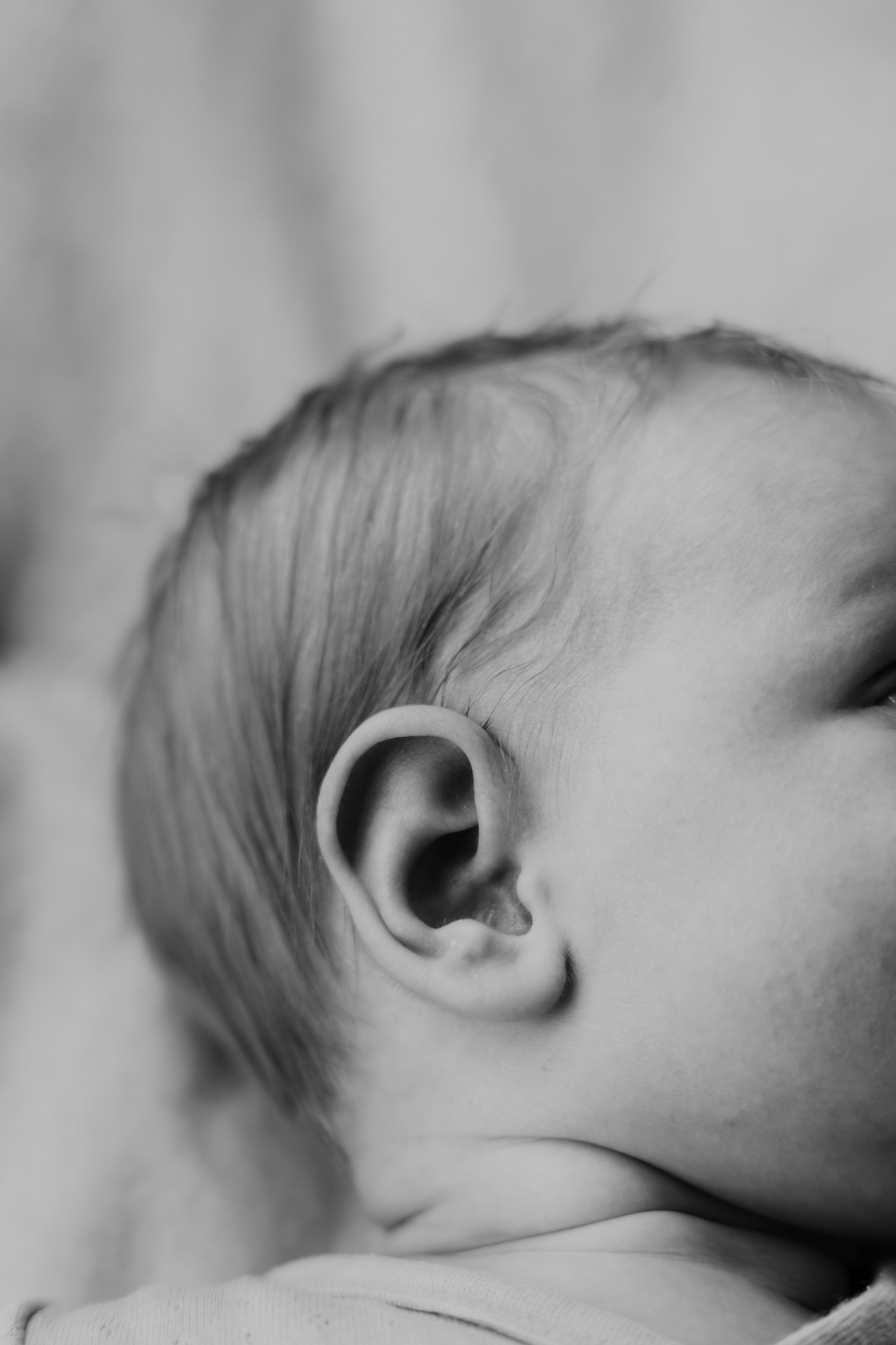 Close-up van een kind dat naar rechts kijkt, zwart-wit foto, focus op oor en haar, onderliggende huid zichtbaar.