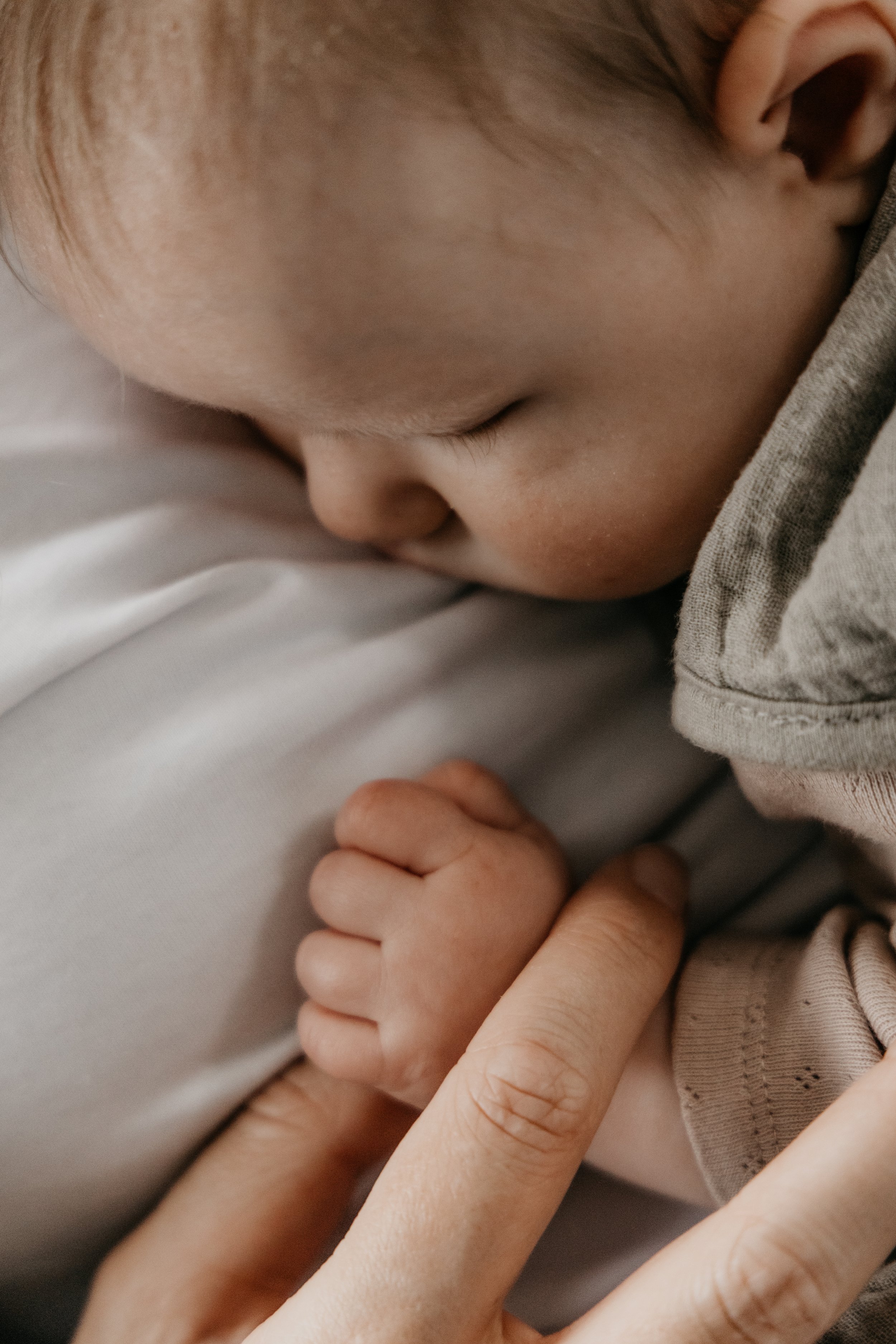 Close-up van een slapende baby die met een volwassen hand wordt ondersteund.