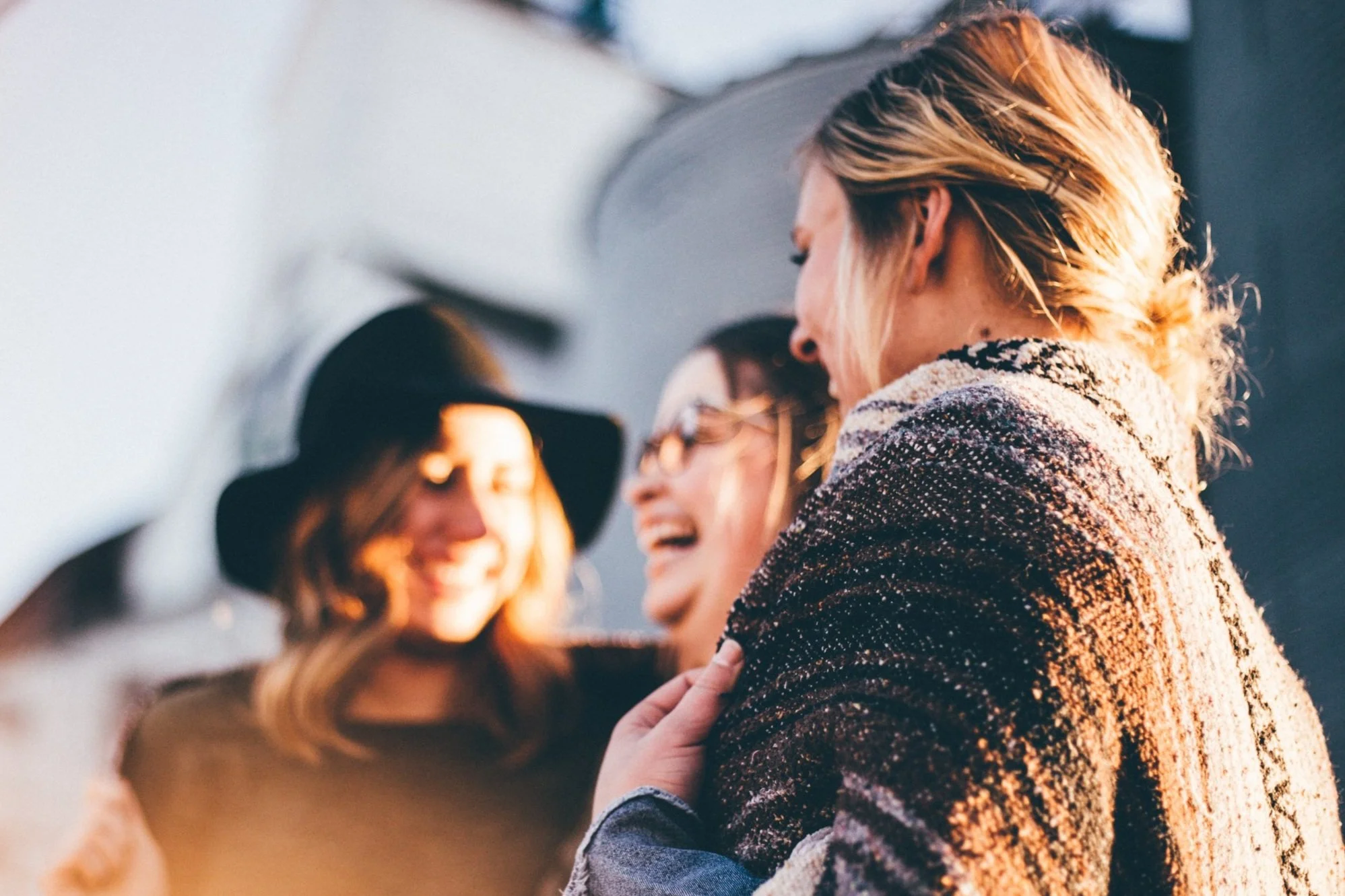 Three women laughing and smiling in sunlight.