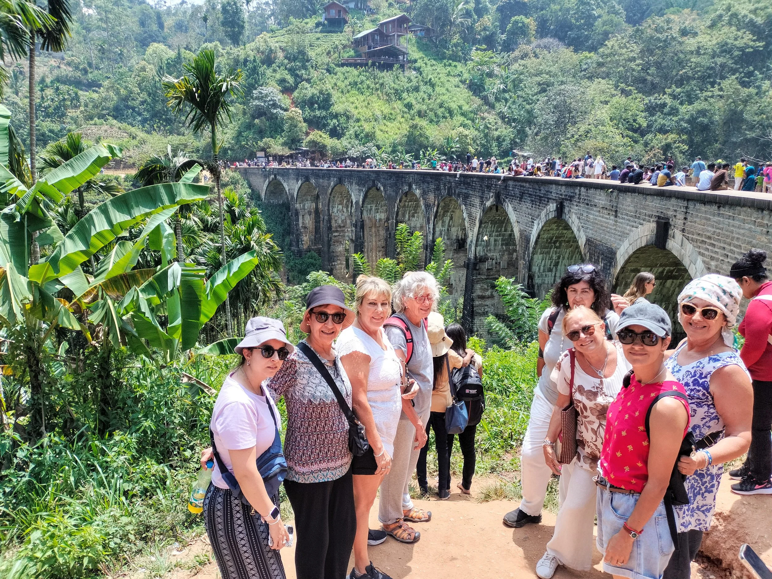 Grupo de turistas en la zona del puente en un paisaje exuberante con vegetación tropical y casas en las colinas.