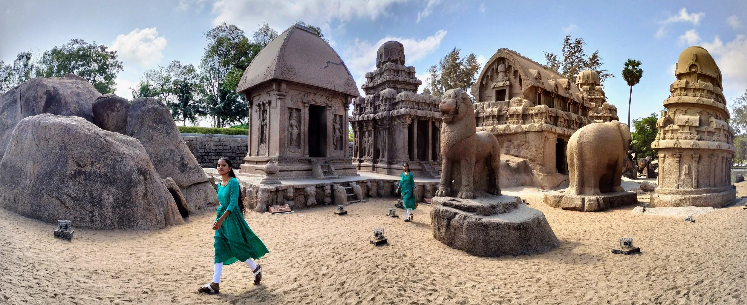Sitio arqueológico con estatuas de piedra, estructuras antiguas y rocas en un ambiente natural con árboles y cielo despejado.
