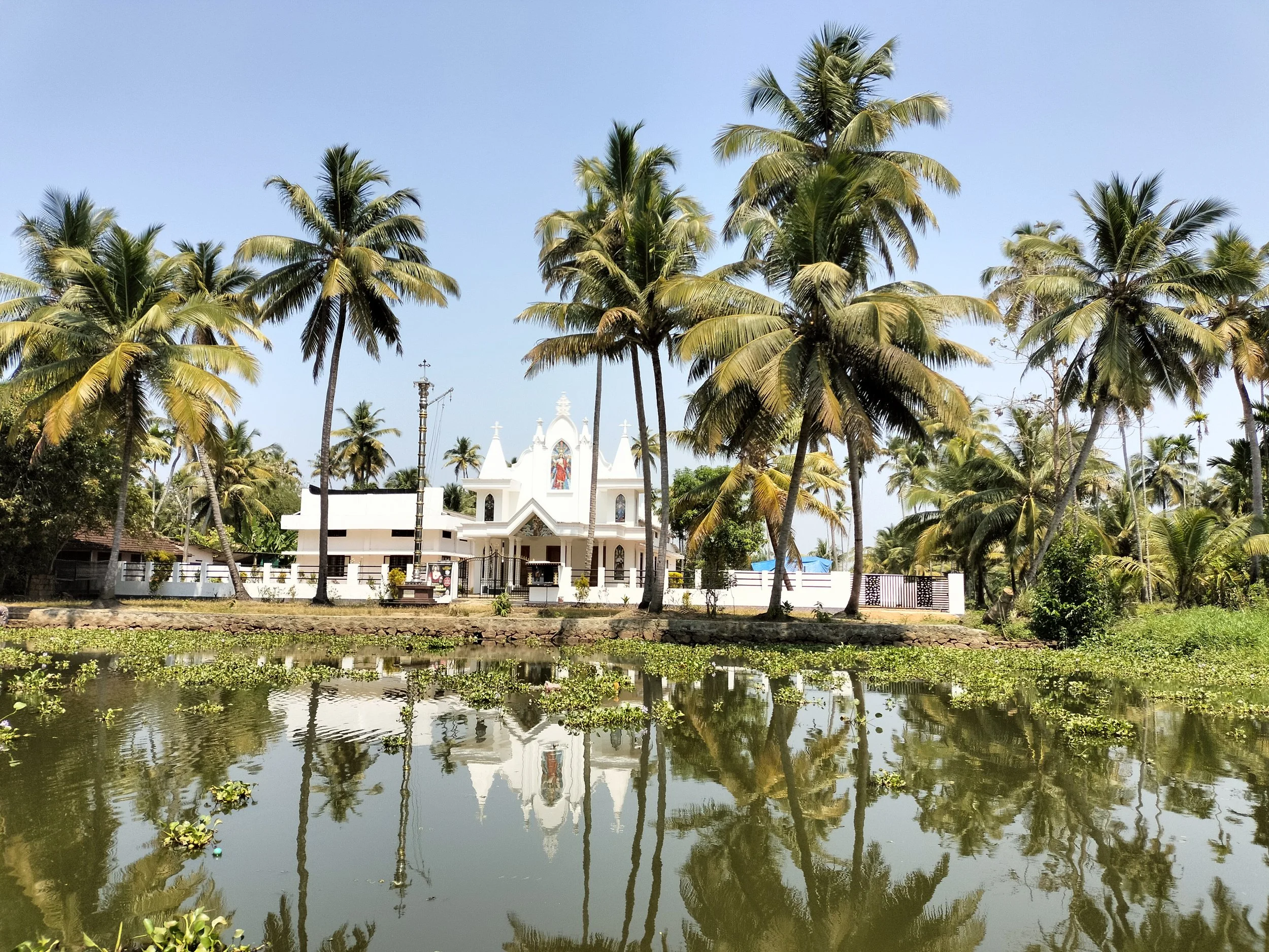Iglesia blanca rodeada de palmeras junto a un cuerpo de agua