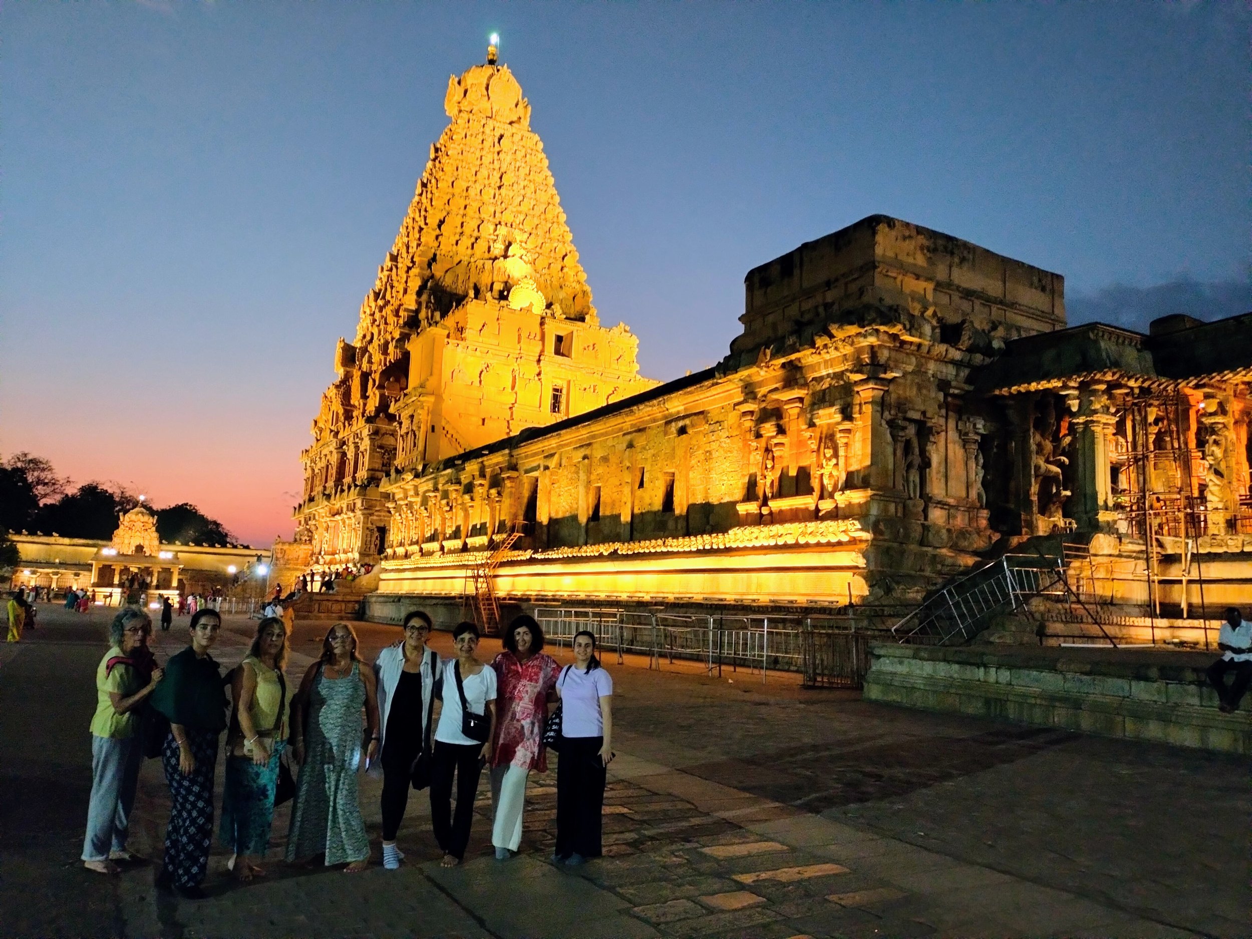 Grupo de personas en el templo de Buda de Mahabalipuram al atardecer, con estructuras antiguas doradas y cielo en tonos de azul y rosa.