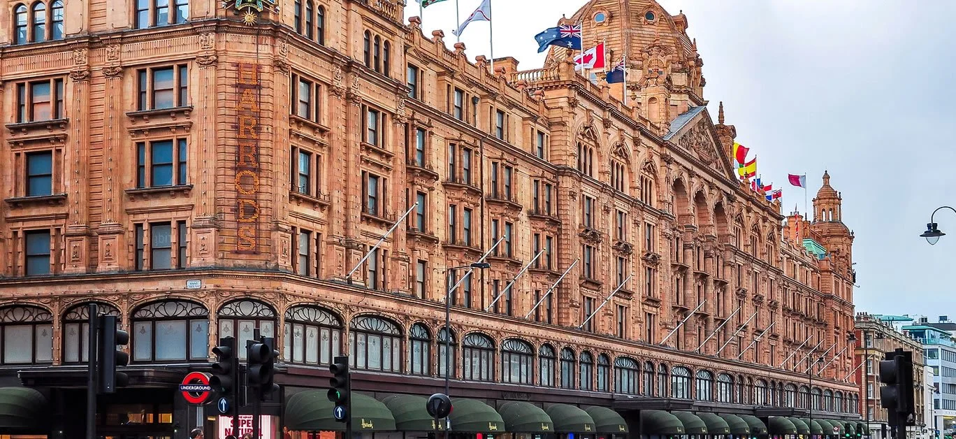 A historic hotel building with a Victorian architectural style, featuring multiple flags on the rooftop, large windows, and street traffic lights below.