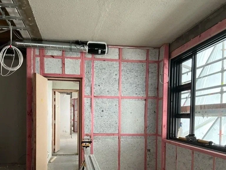 Interior under construction showing wall insulation, double glazed windows, and ventilation ductwork being installed.