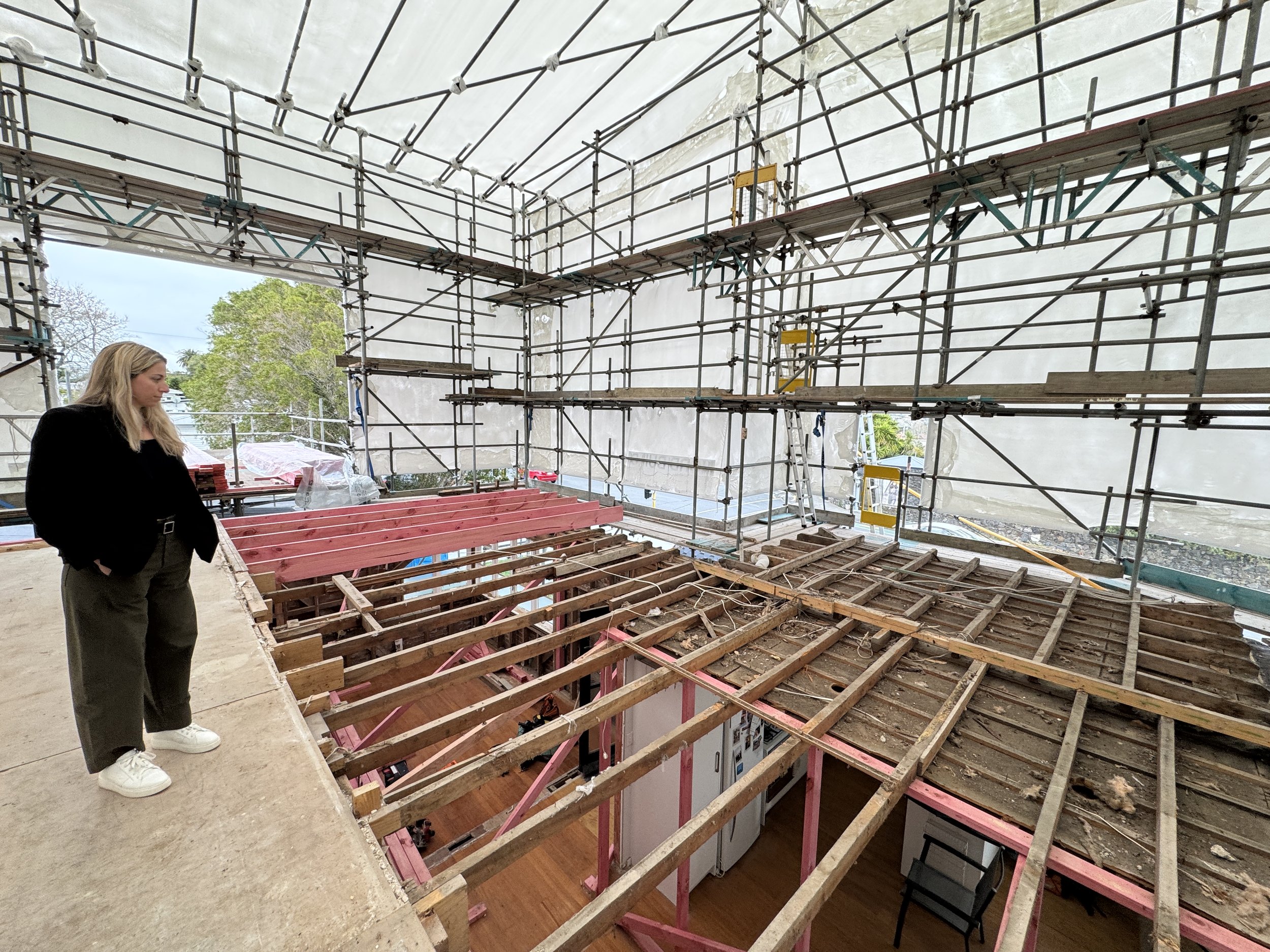 Client experiencing the construction process firsthand, seeing their home renovation take shape as existing floor framing is exposed and new structural work progresses.