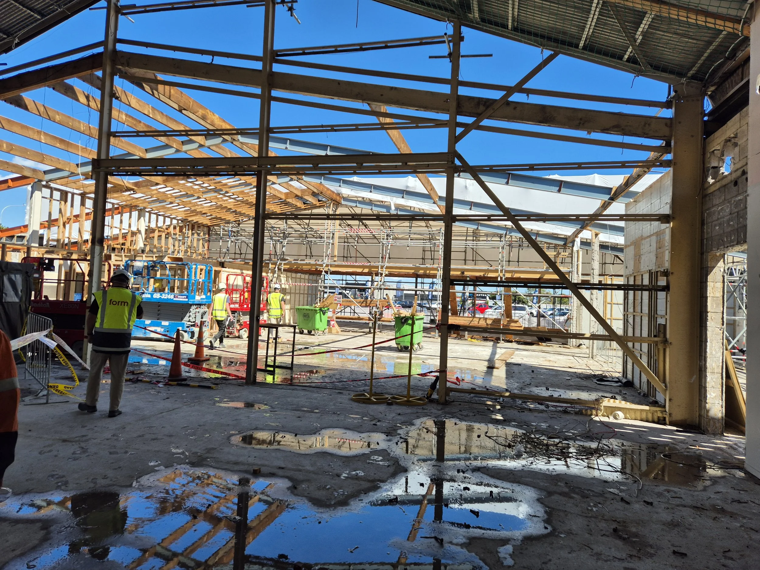 Existing building under construction with exposed structure, water on slab, and partially demolished elements, highlighting unknown site conditions uncovered during works.