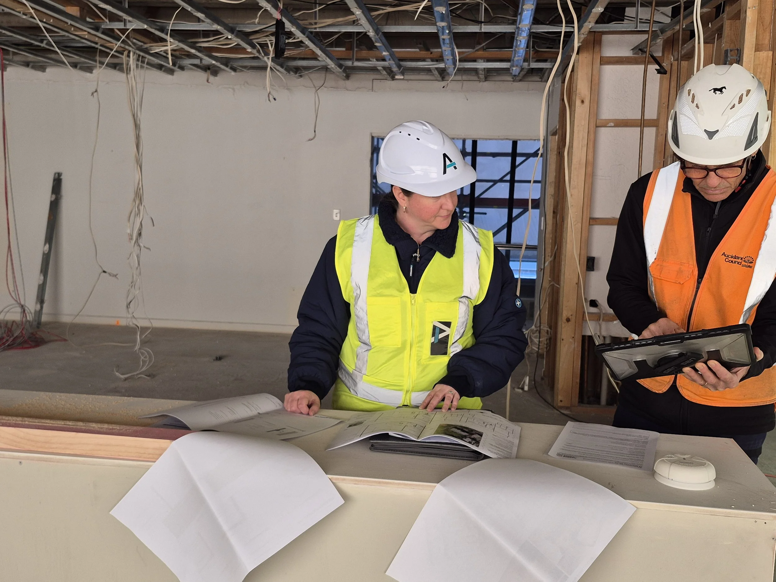 Architect and building inspector reviewing architectural drawings during a construction site visit.