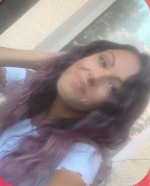 A young woman with long dark hair and purple highlights taking a selfie outdoors.