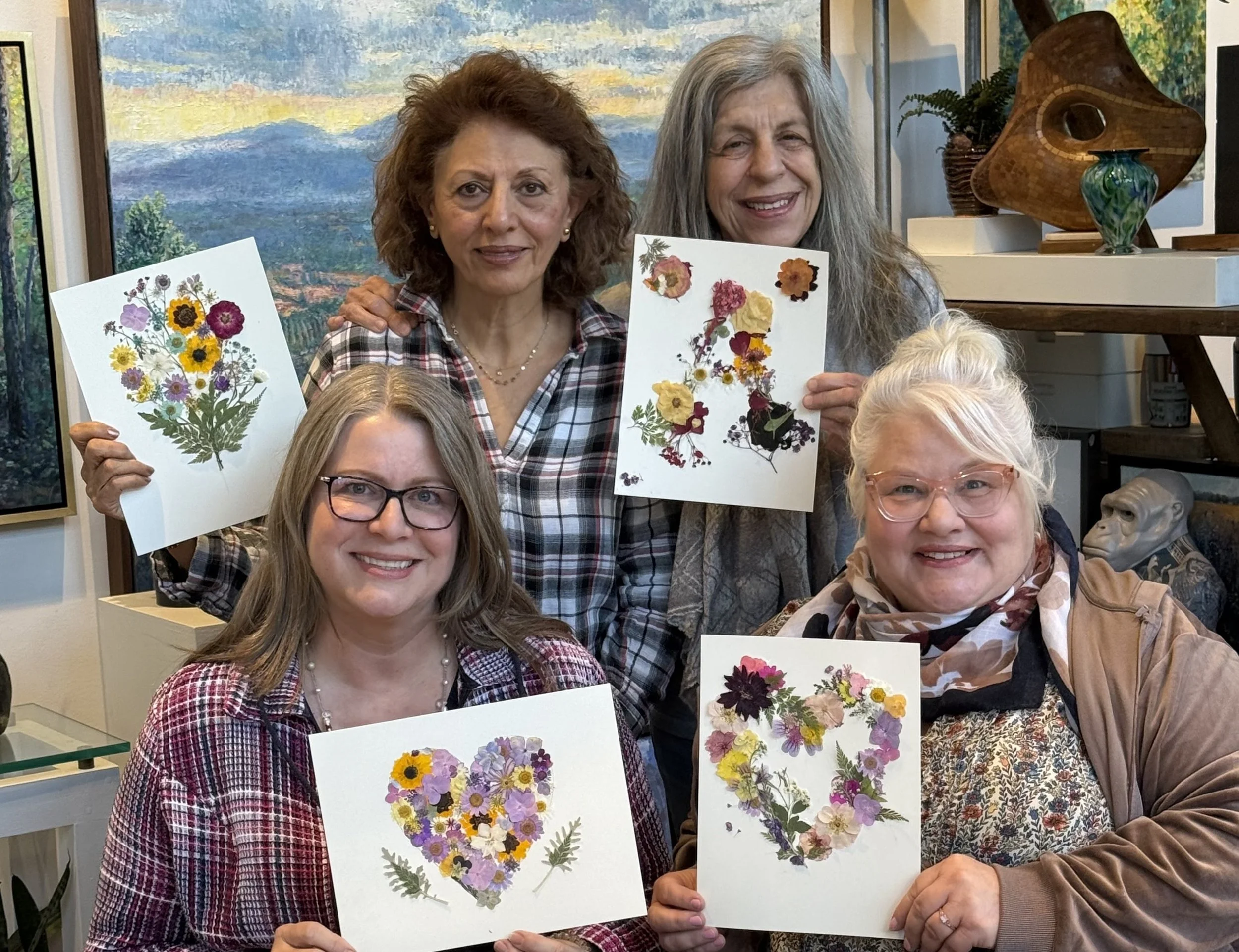 Two men painting landscape scenes on small canvases at an art studio with colorful paintings on the walls. One man is in the foreground, focusing on their work, while the other is in the background, painting on an easel.