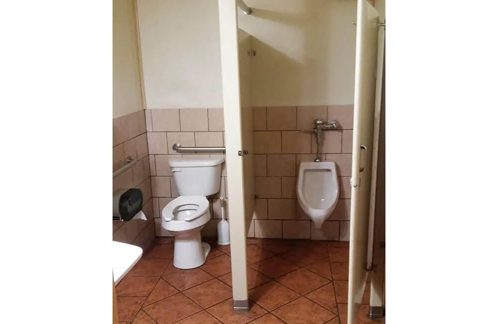 Public restroom with a toilet, urinal, and stall with a partition in a tiled bathroom