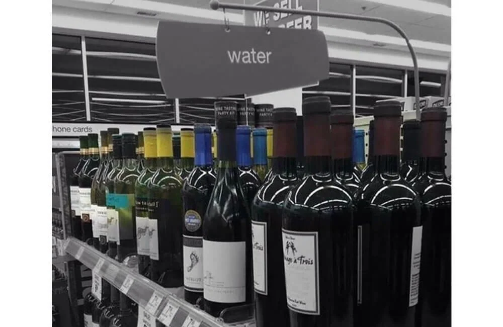 Shelves of wine bottles with a sign that says "water" hanging above.
