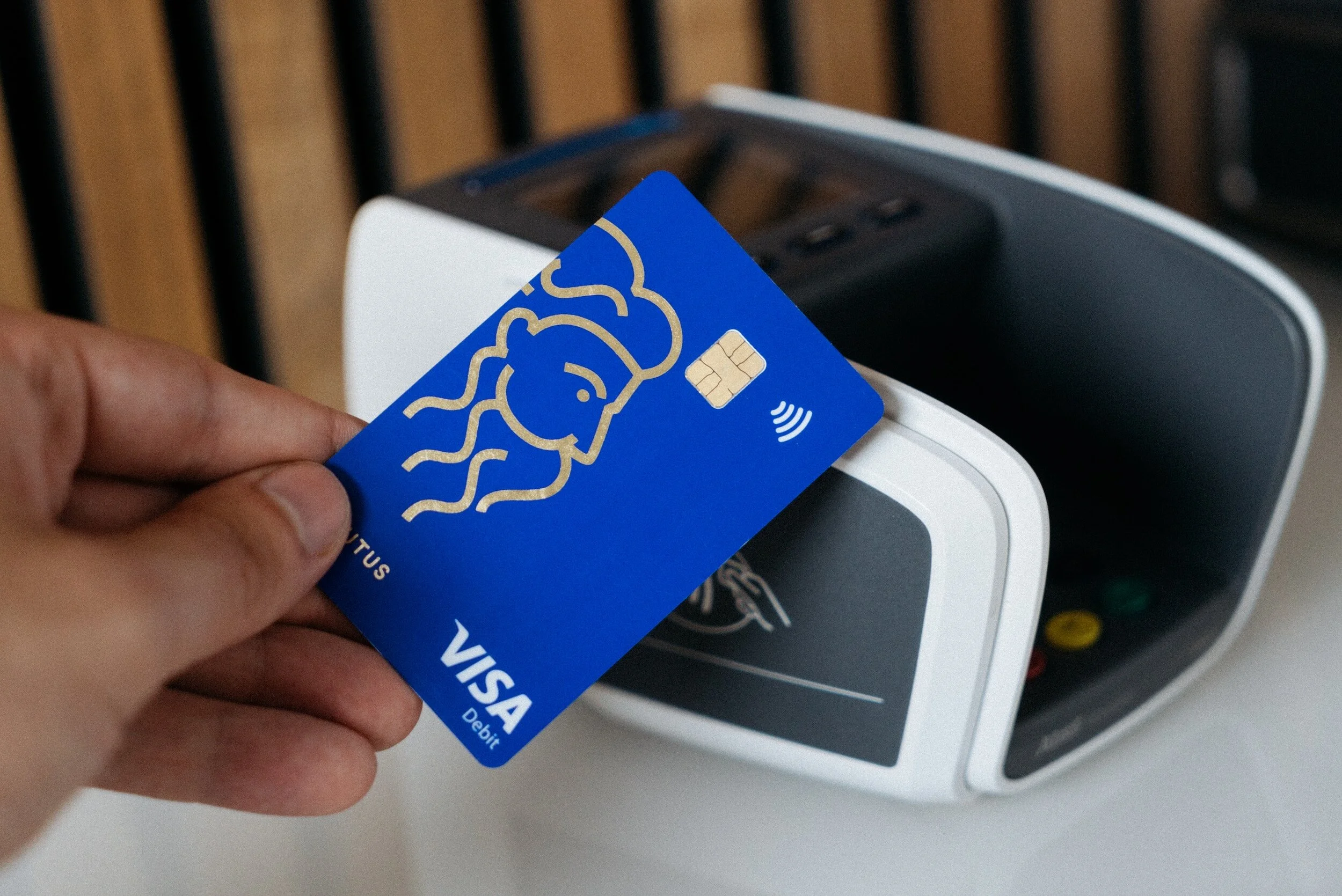 A person holding a blue VISA debit card near a contactless payment terminal.