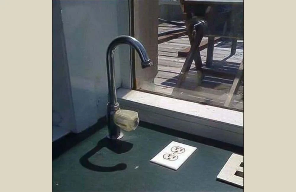 A kitchen sink faucet with a wrapped sponge hanging from it, positioned in front of a window with a view of an outdoor deck.