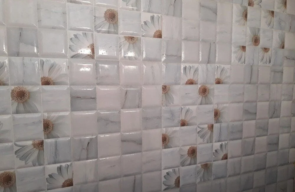 Close-up of a wall covered with white and beige floral patterned ceramic tiles.