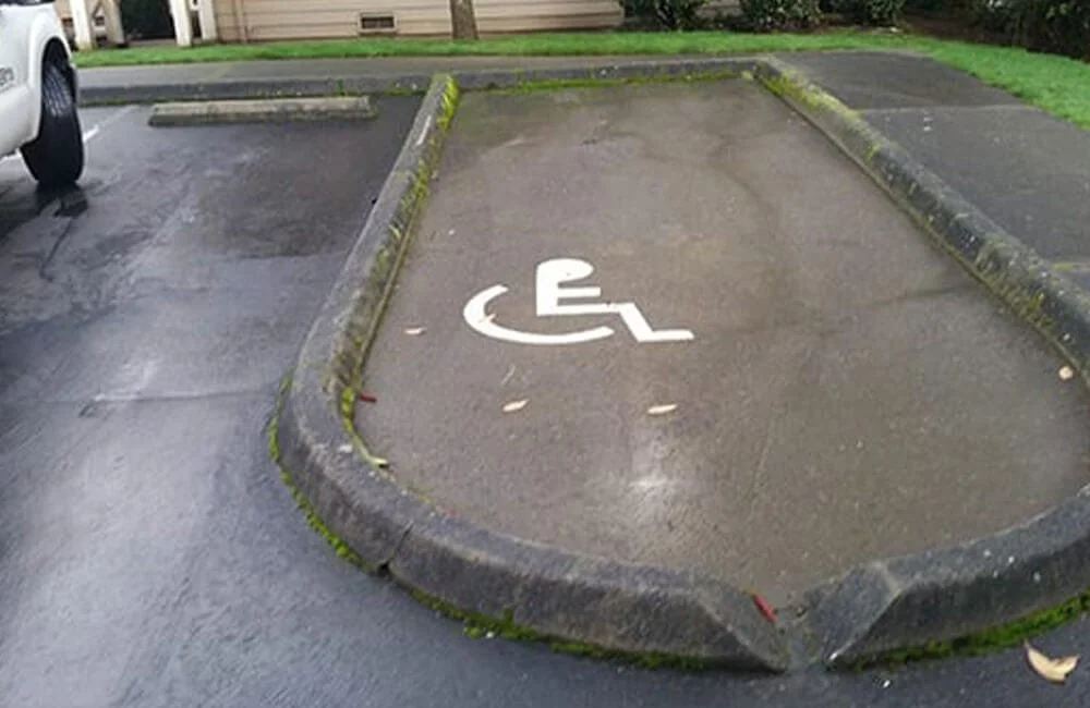 Empty handicapped parking space with white wheelchair symbol, surrounded by concrete curbs, in a parking lot.