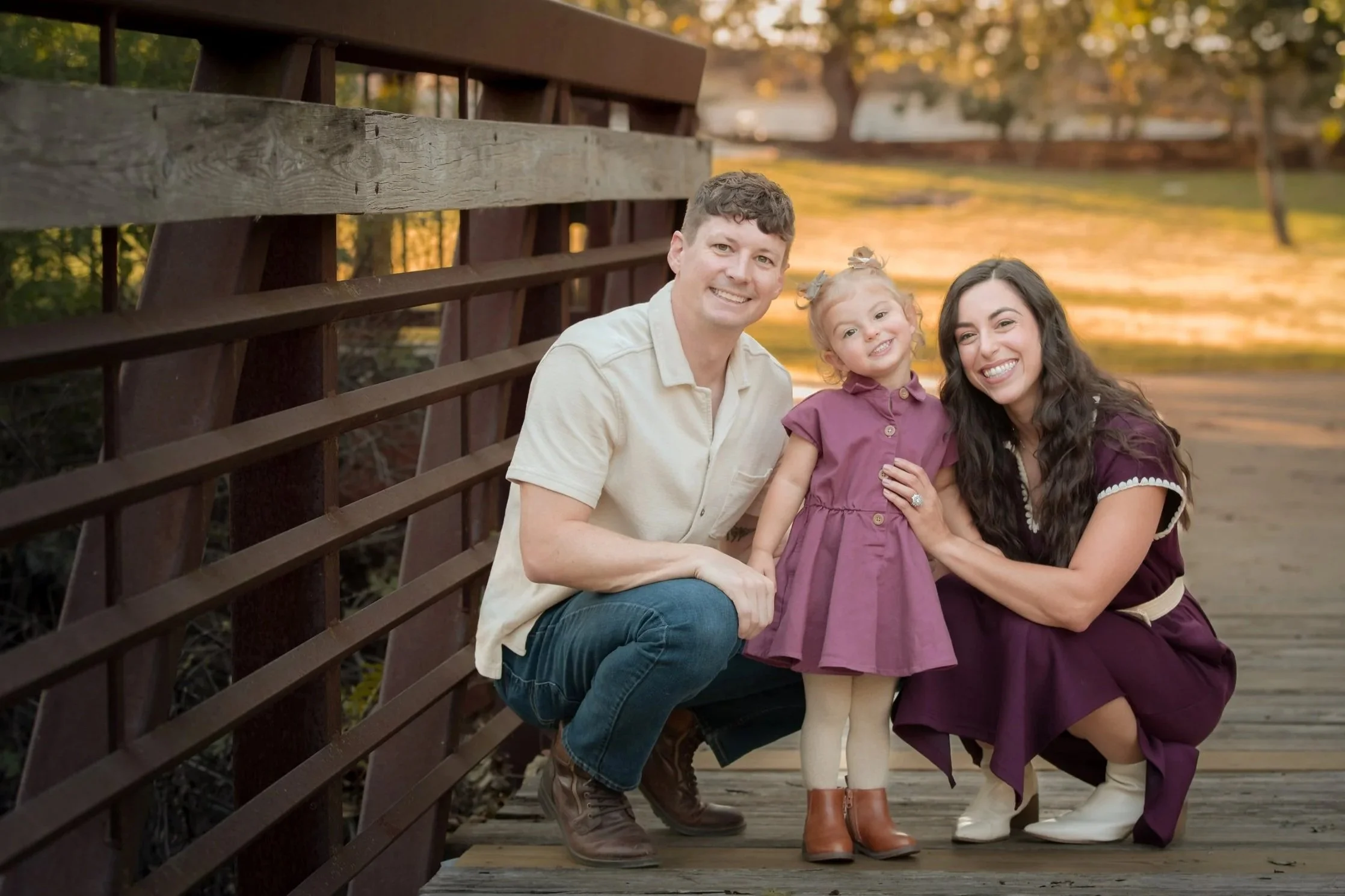 Family of 3, mom, dad and 2 year old daughter, standing close on a bridge during an outdoor  family photo session in Elmer Oliver Nature Park in Mansfield, TX