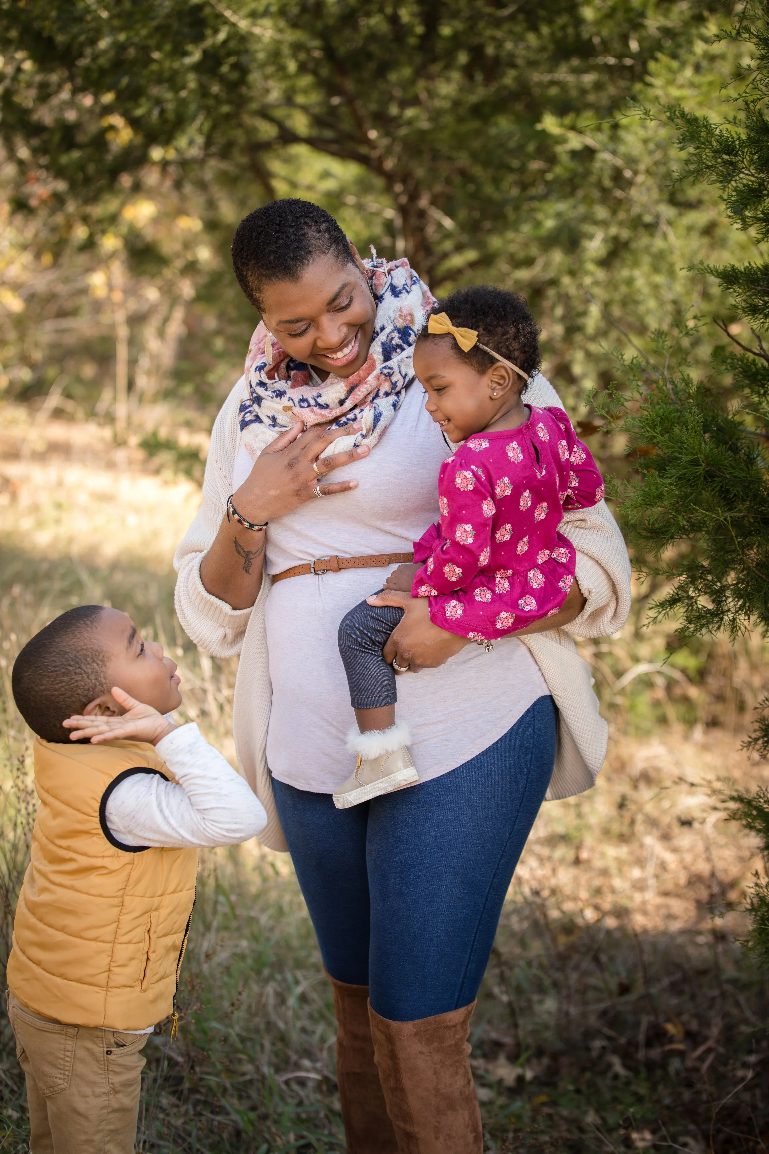 African-American family of three smiling at each while posing for family photos in a park.