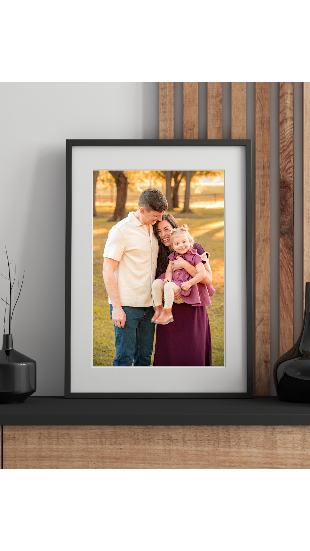 Family photo of a dad with mom holding little girl, in a black frame sitting on a shelf