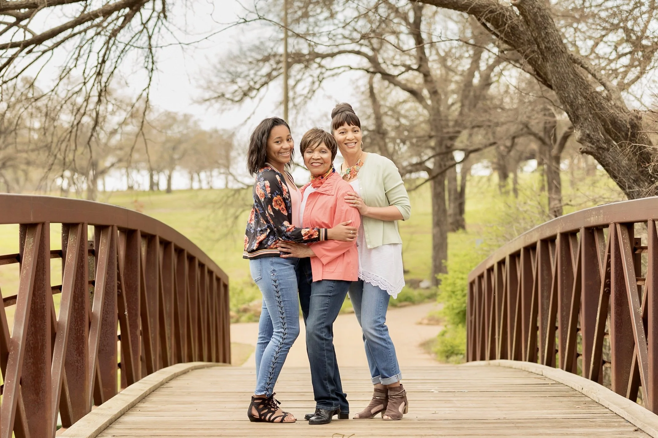 Three generations of African-American women, grandmother, mom and teenage girls, posing on a bridge in a park.