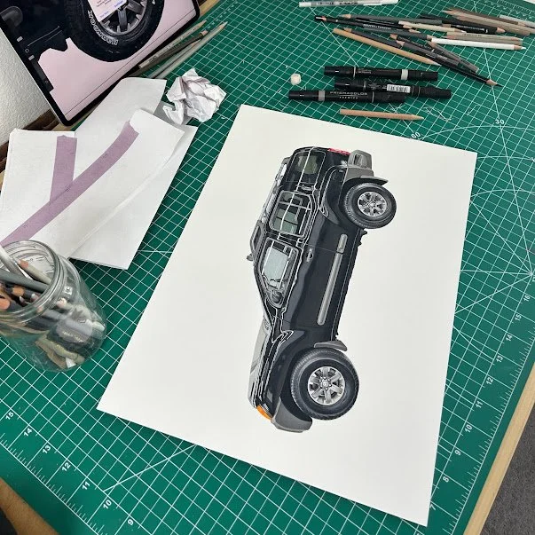 A work table with drawing supplies, including paintbrushes, markers, and paper, with a detailed car illustration on paper.